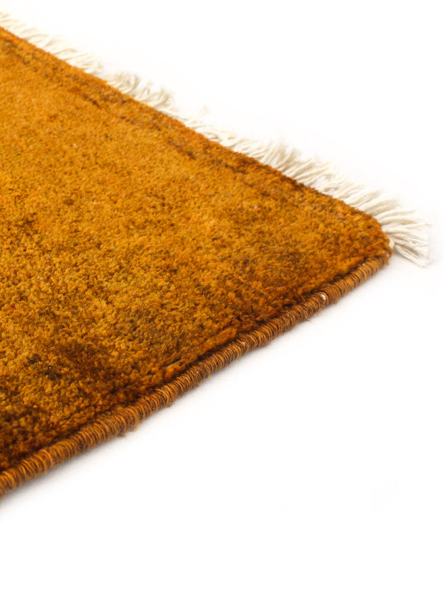 Close-up of the corner of the catalog:three Overdyed Rug in Safron (193 x 261 cm), featuring hand-knotted orange wool with white fringe, shown on a white background.