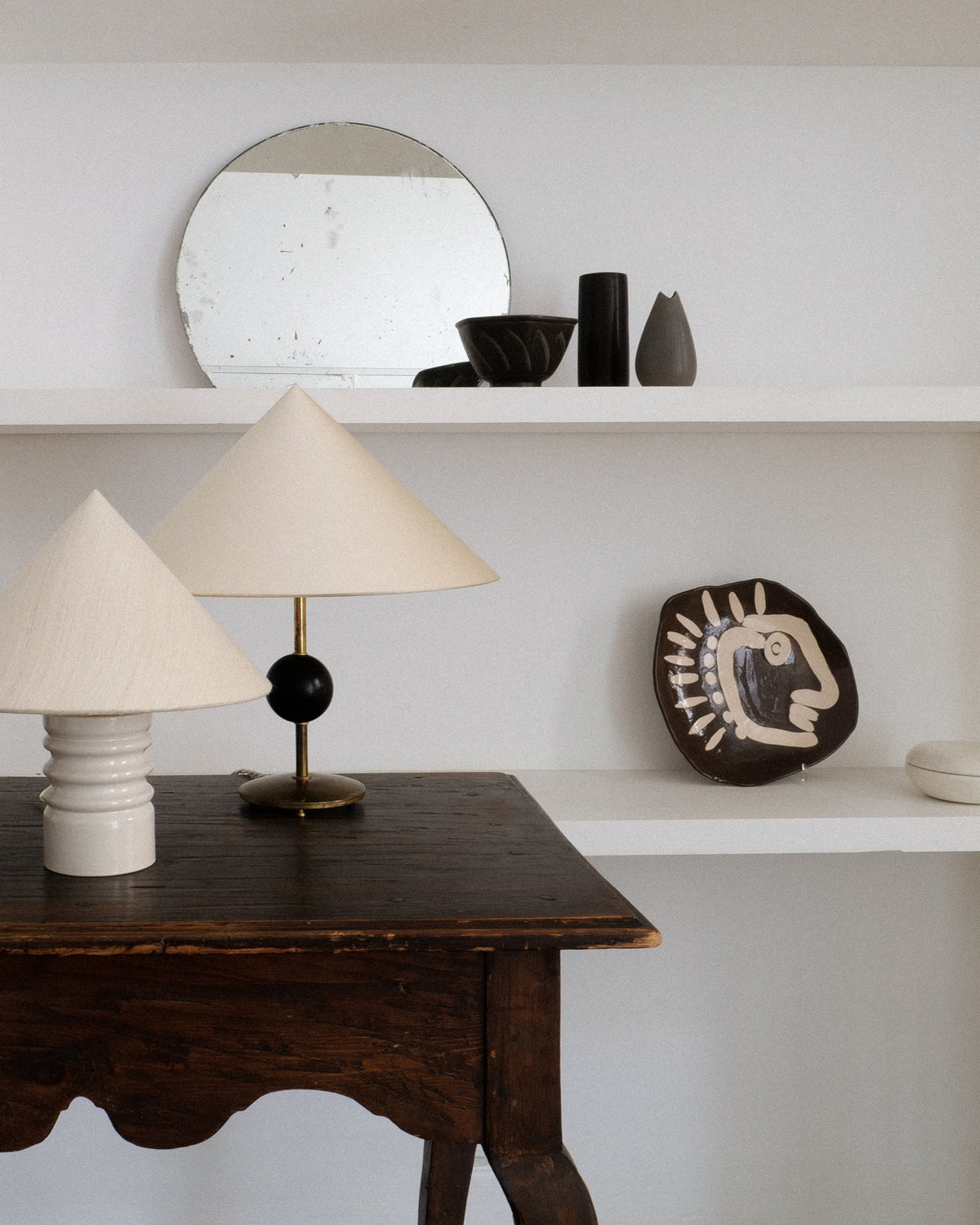 Modernist ceramic plate styled with vintage lamps on wooden desk
