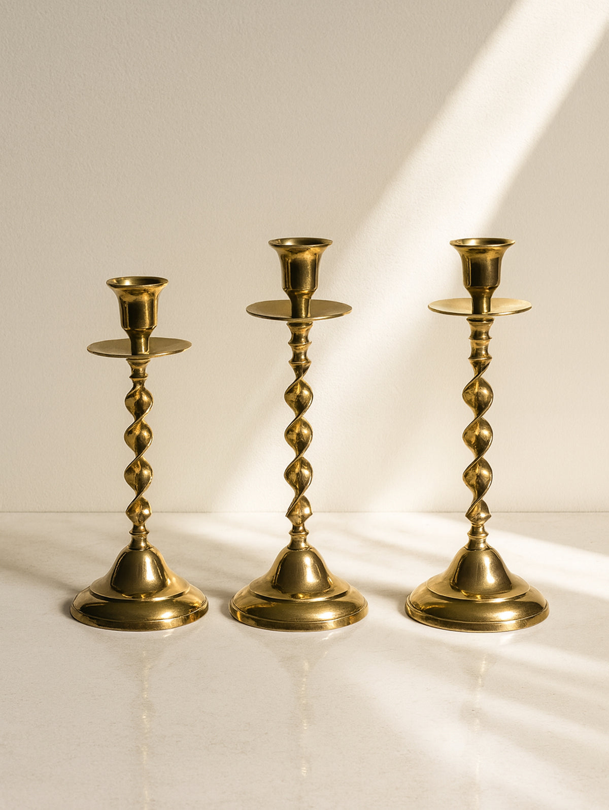 Three brass candlesticks with twisted stems on marble surface
