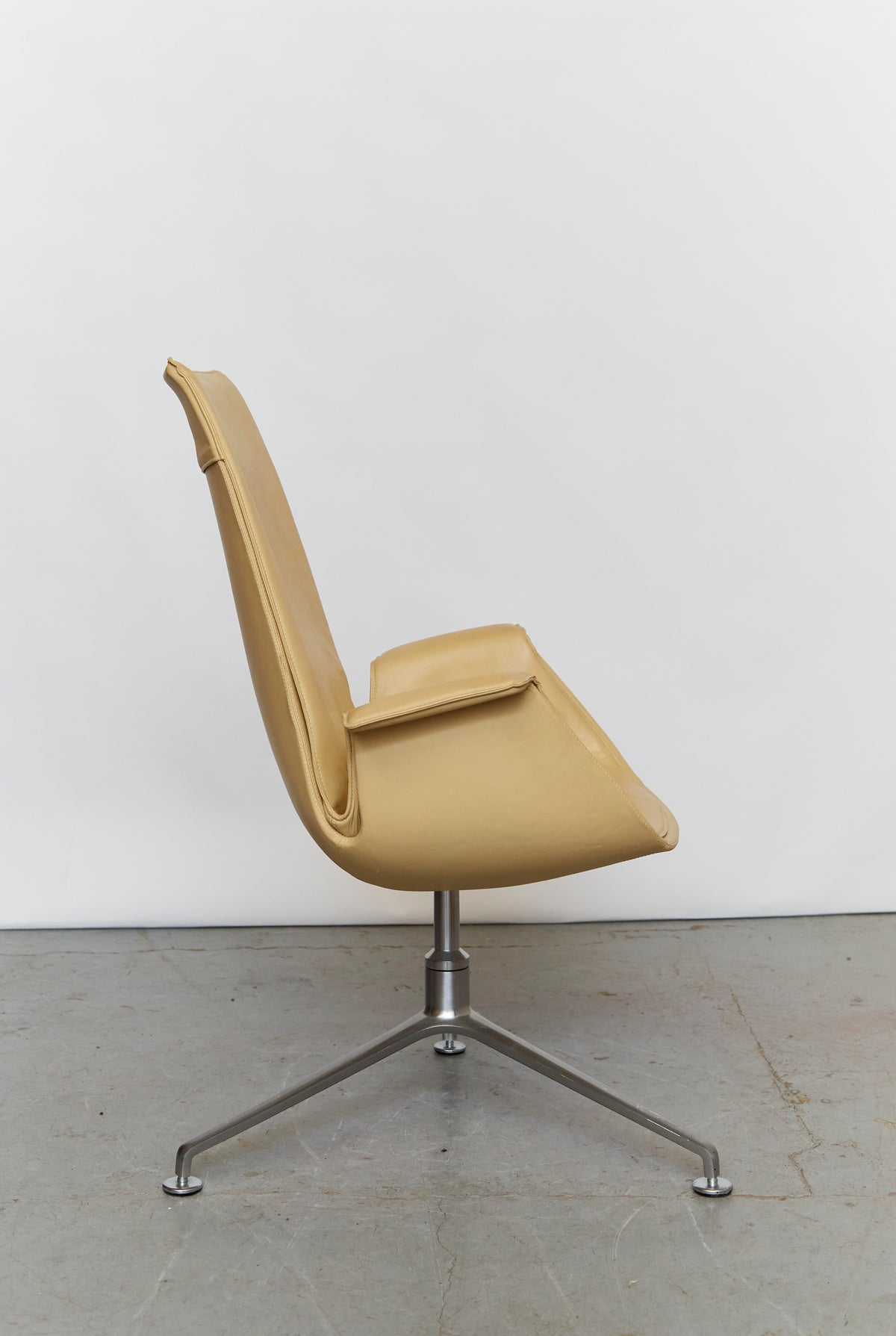 Side profile view of beige leather swivel tulip chair with metal base