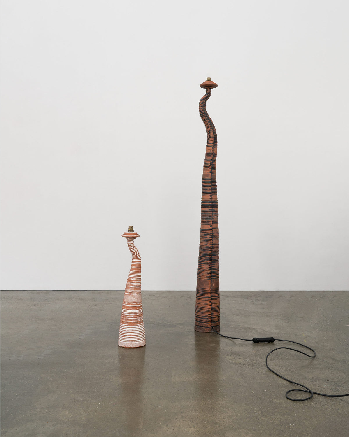 Two sculptural terracotta lamps with curved necks in gallery setting