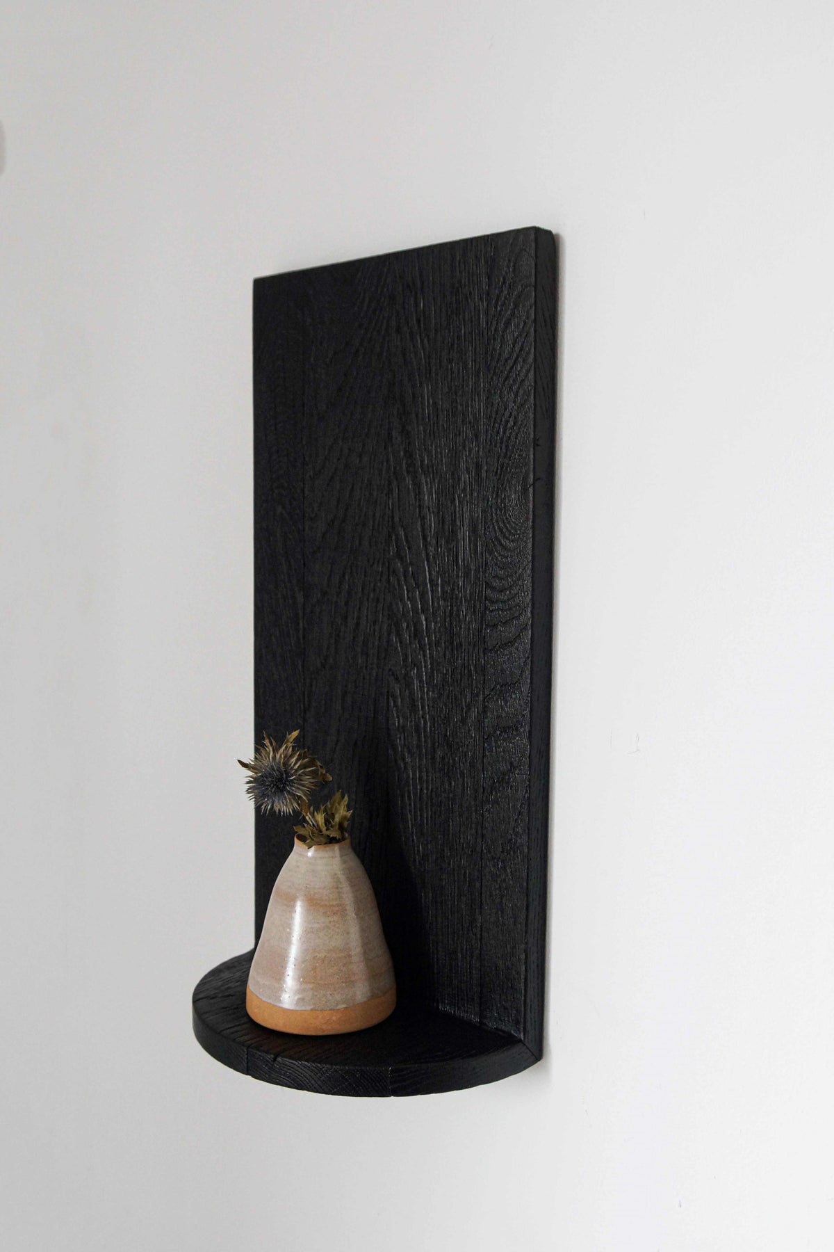 The Megaron - Minimalist Shelf in Wood (Small) by COSEINCORSO displays a small ceramic vase with dried thistle flowers, bringing minimalist charm to a plain white wall.