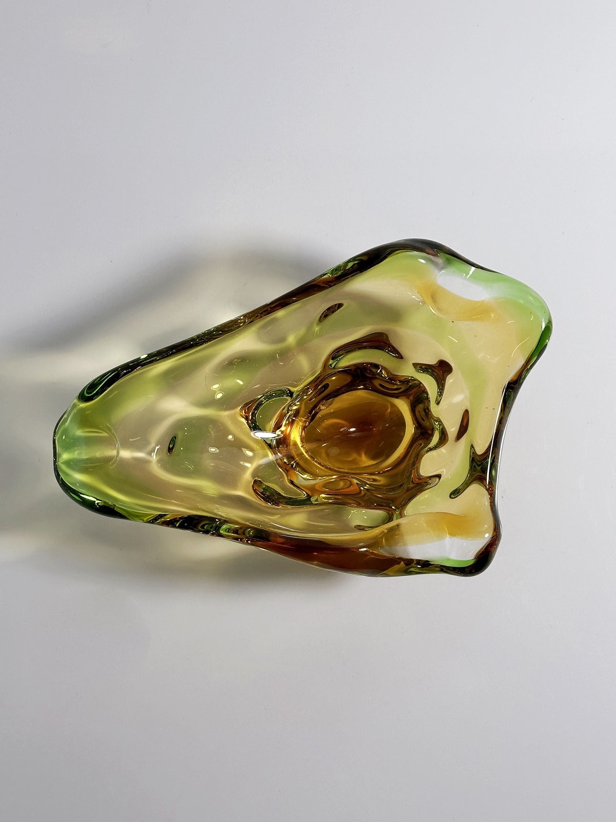 The Bohemian Vide-poche by Dodo Vintage (1960s) features sculptural glass with swirling green, yellow, and amber hues, an organic asymmetrical shape, and smooth edges, shown from above on a plain white background.