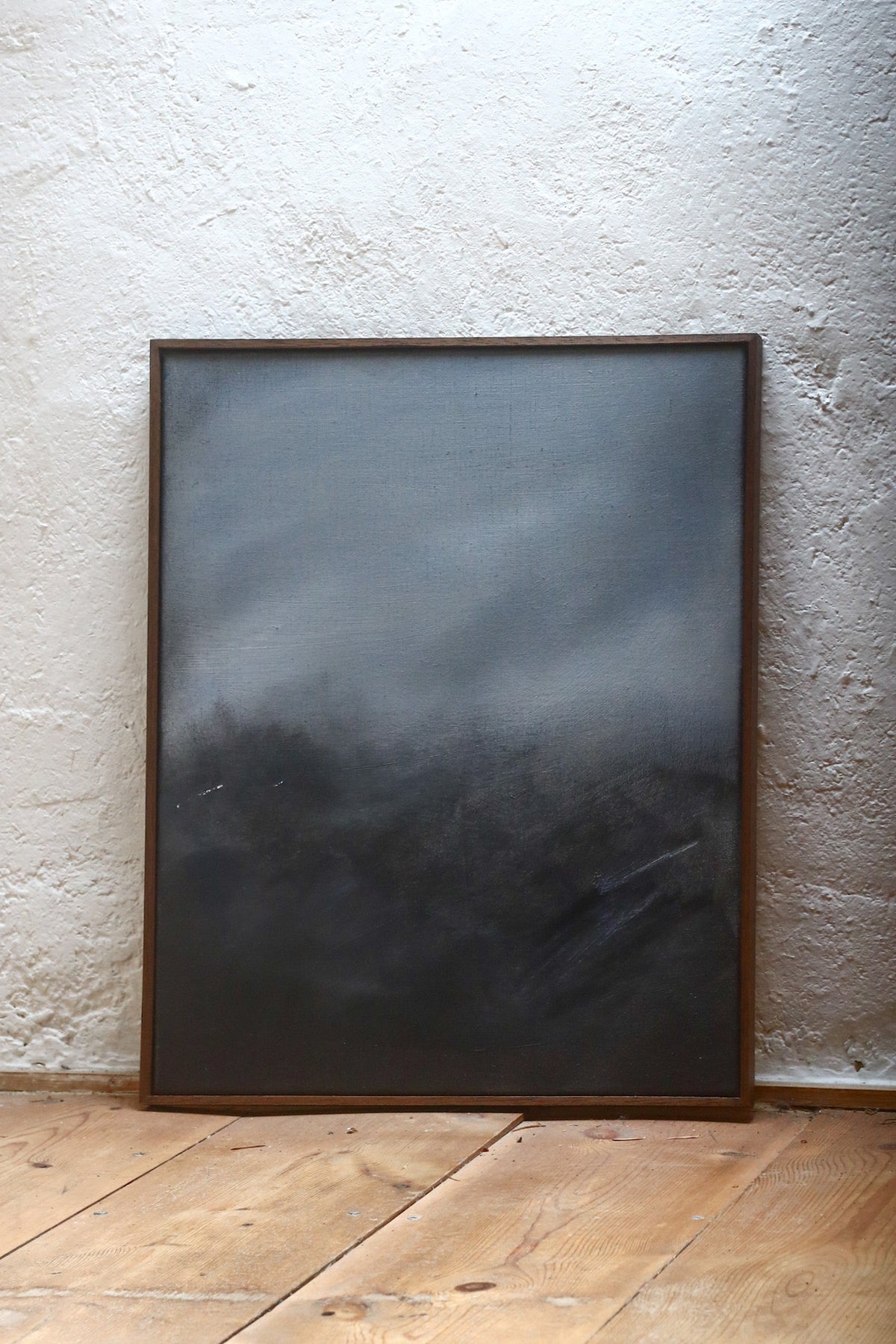 As Night Draws In" by David Hardy is an original acrylic on linen featuring a moody, misty abstract landscape in smoky gray and black tones, displayed against a textured white wall on a wooden floor.