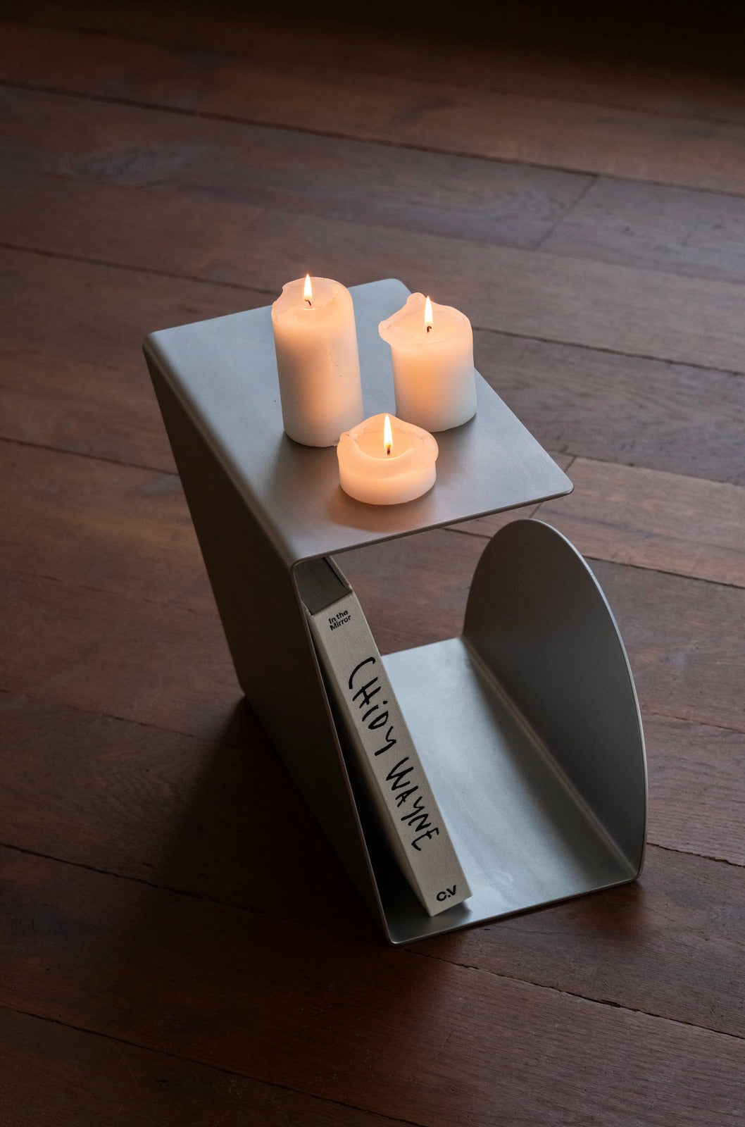 Side Table - 1.0 - Stainless Steel — top view with candles and book on wood floor