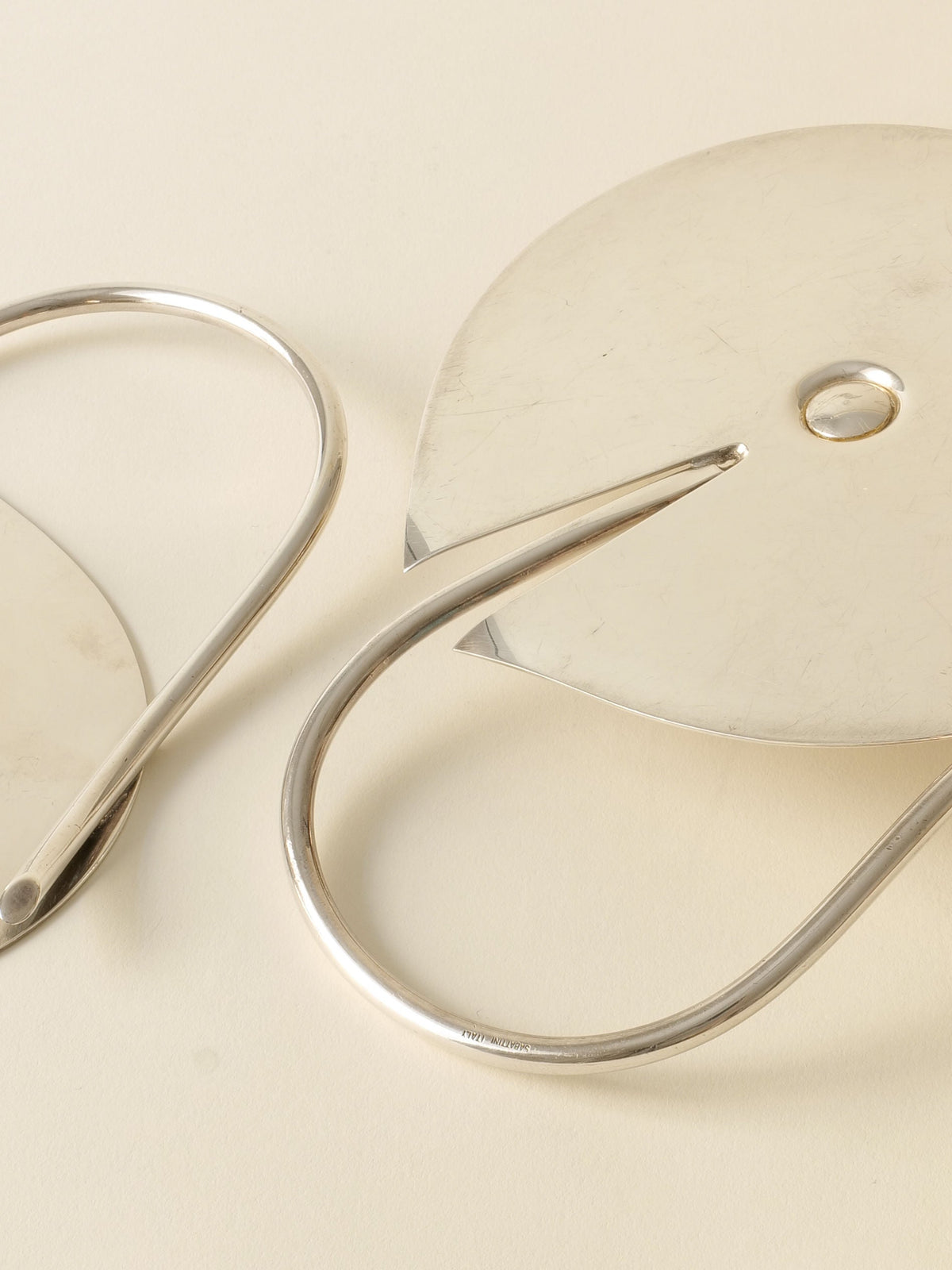 Two Candle Holder Lino Sabattini 1970s by Collection apart, with sleek curved design and metallic finish, rest diagonally on a light surface. Their stylish look evokes modern Italian elegance.