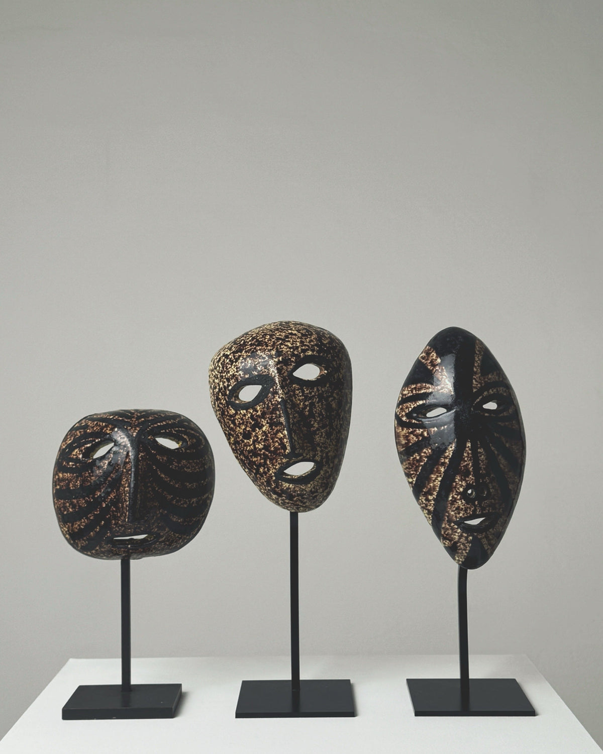 Three black ceramic masks with gold speckled patterns on stands