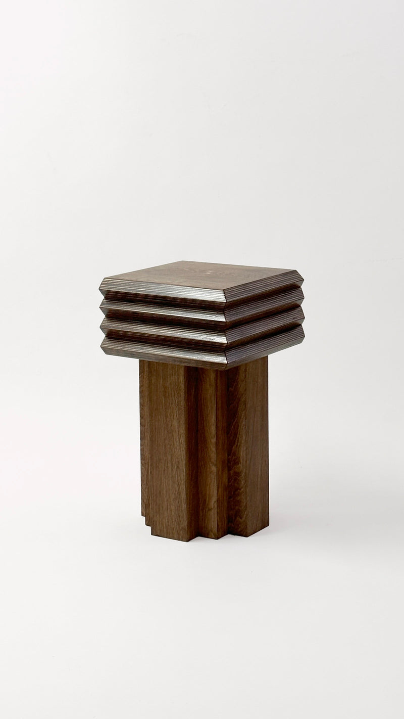 The MM Stool - Dark Oak by GOONS is a modern wooden stool with a square, layered seat featuring beveled edges and a base of four grooved vertical segments, designed in Paris and shown against a plain white background.