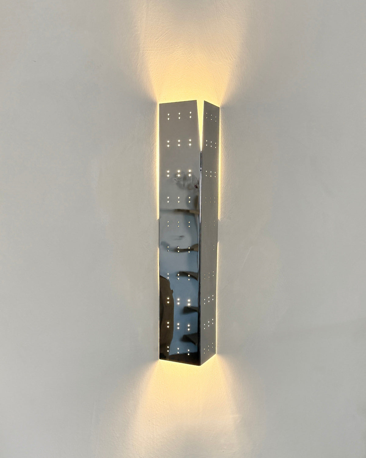 May Wall Lamp - Polished Steel — side angle showing reflective surface on wall