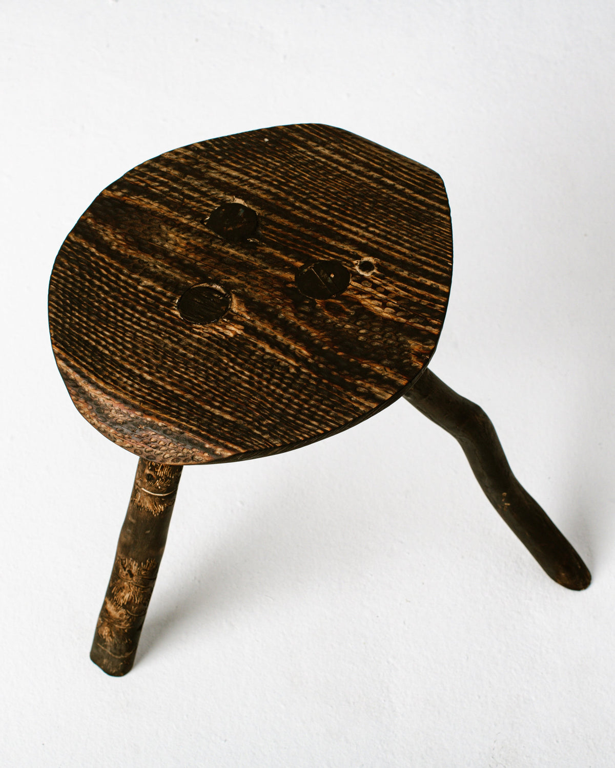Three-legged burned wood stool with charred texture detail