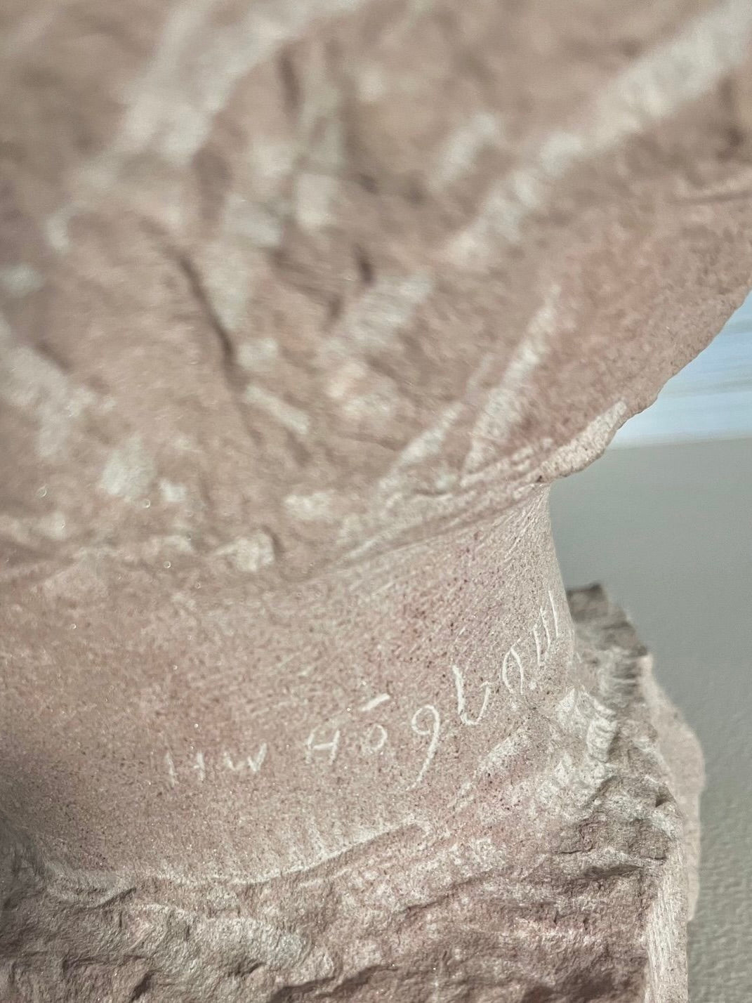 Close-up detail of stone bust sculpture showing carved signature