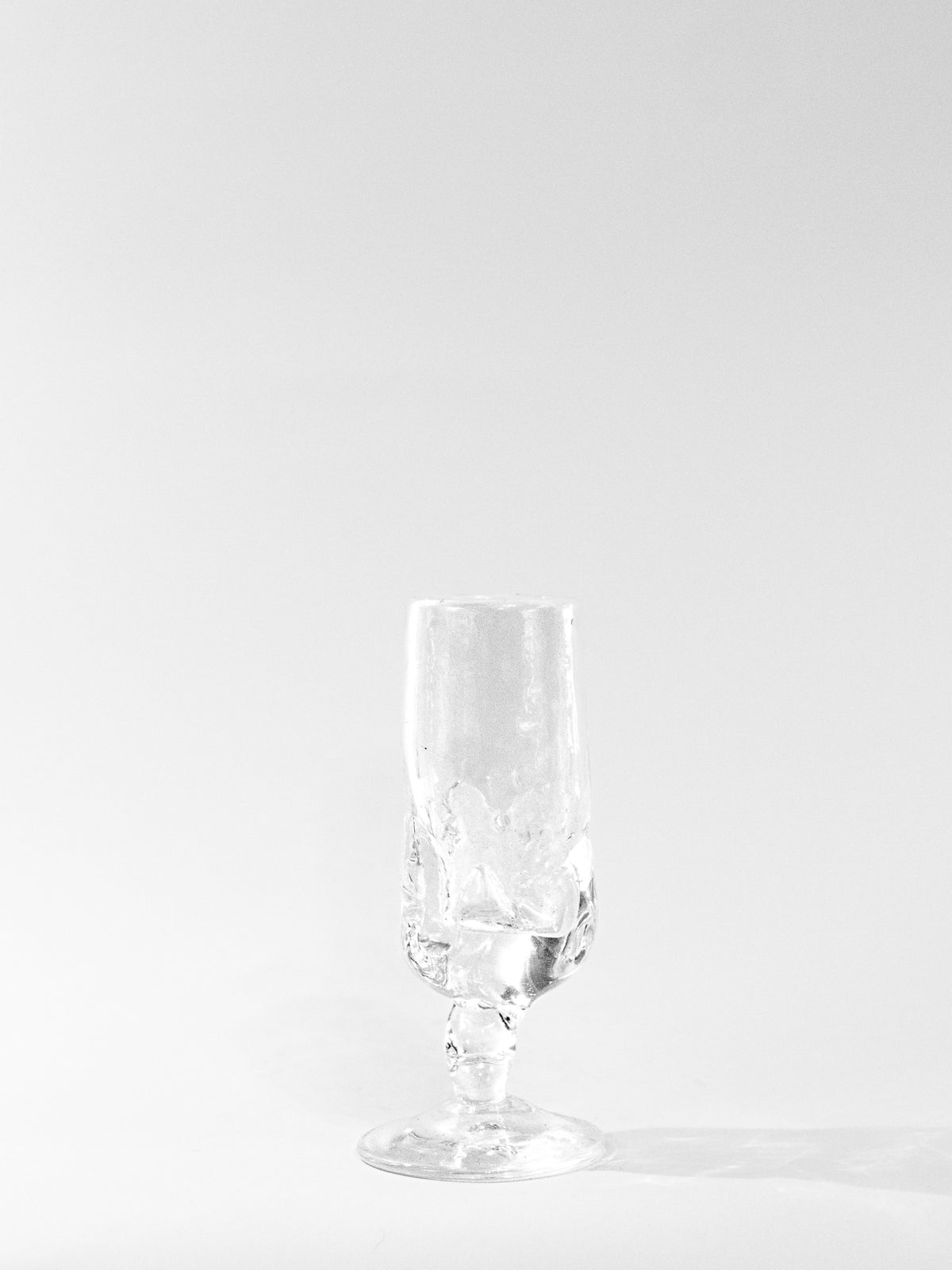 A clear, empty Table Goblet by Szkło Studio with a textured surface stands on a plain white background, casting a soft shadow. The minimalistic, well-lit image highlights the craftsmanship of Szkło Studio.