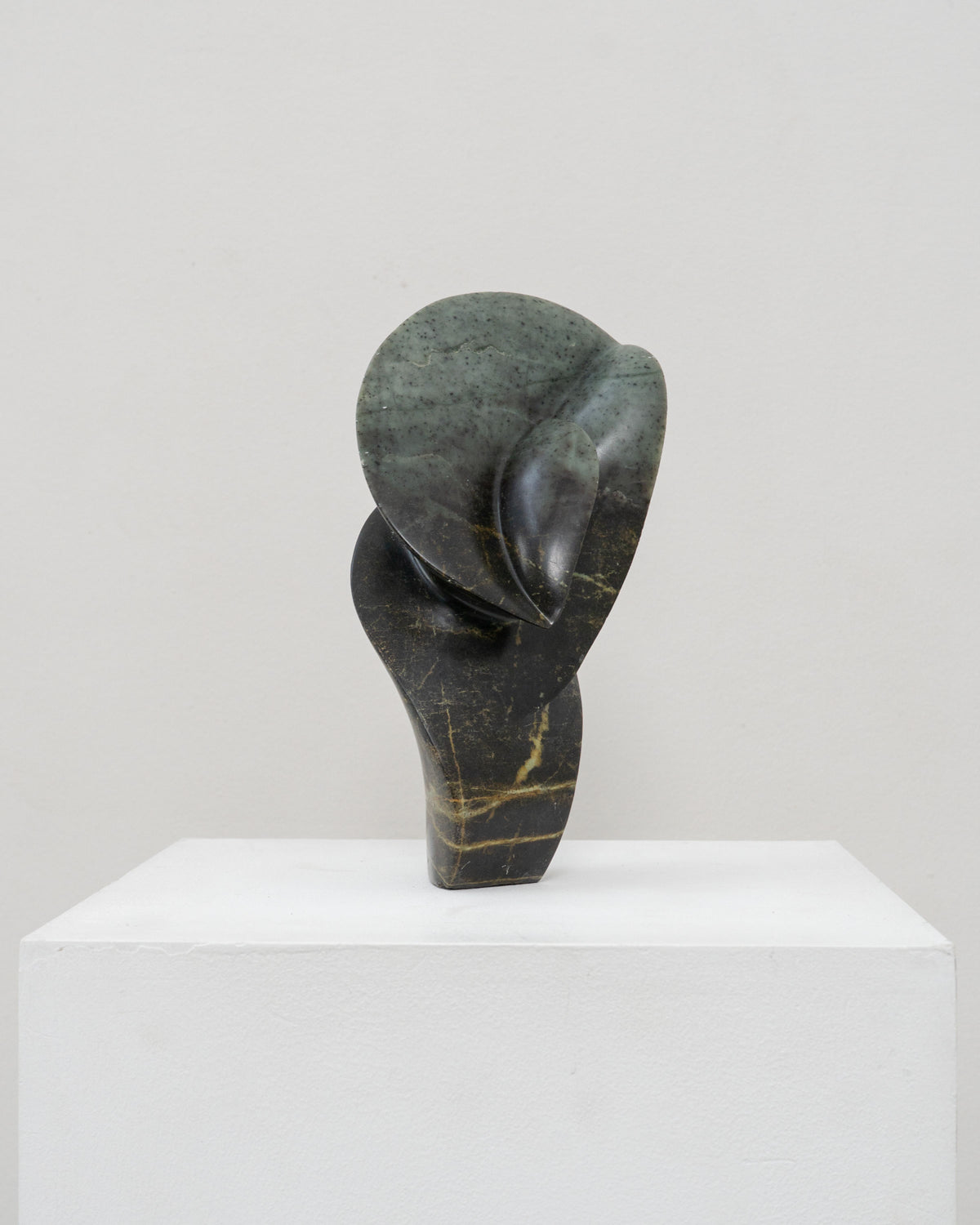 Abstract stone sculpture with curved organic form on white pedestal