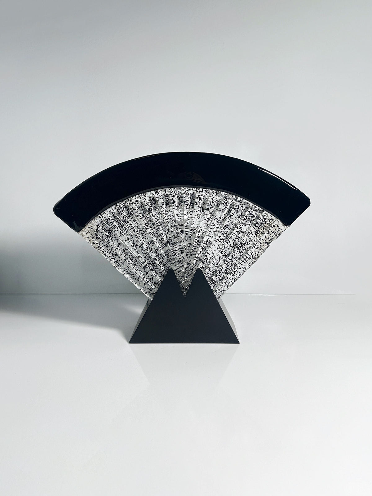 The Large Murano glass fan lamp by Dodo Vintage features a modern abstract Art Deco design, with a black fan-shaped arc and textured silver crescent on a geometric black triangular base, displayed on a reflective white surface.