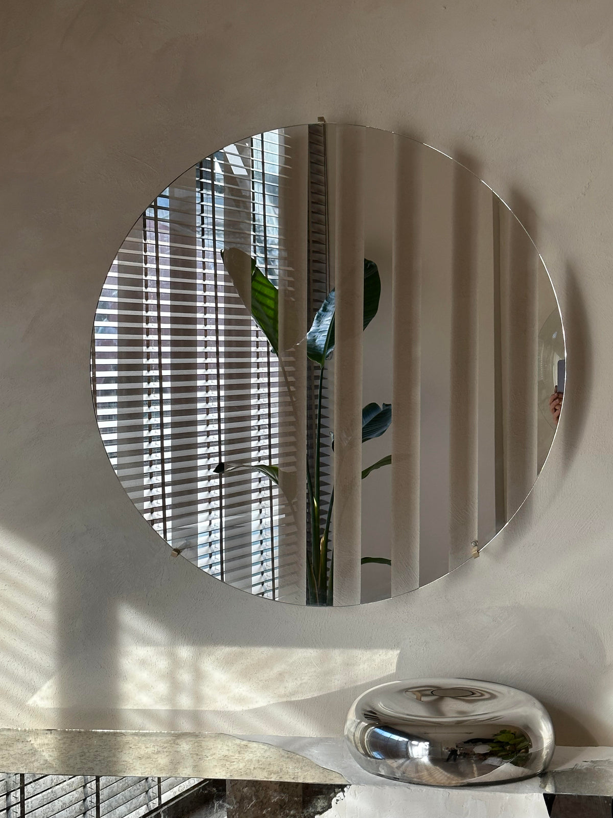 Line III Mirror — round mirror reflecting indoor plant and blinds