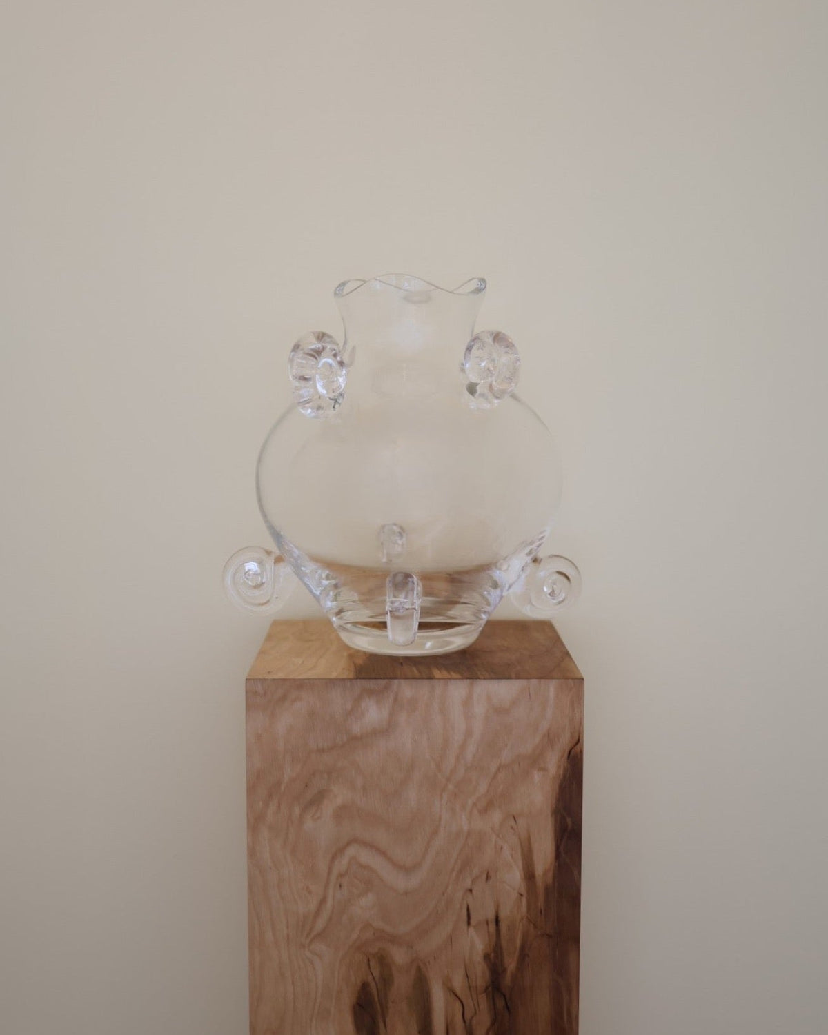 Clear crystal vase with rounded body and ears on wooden pedestal