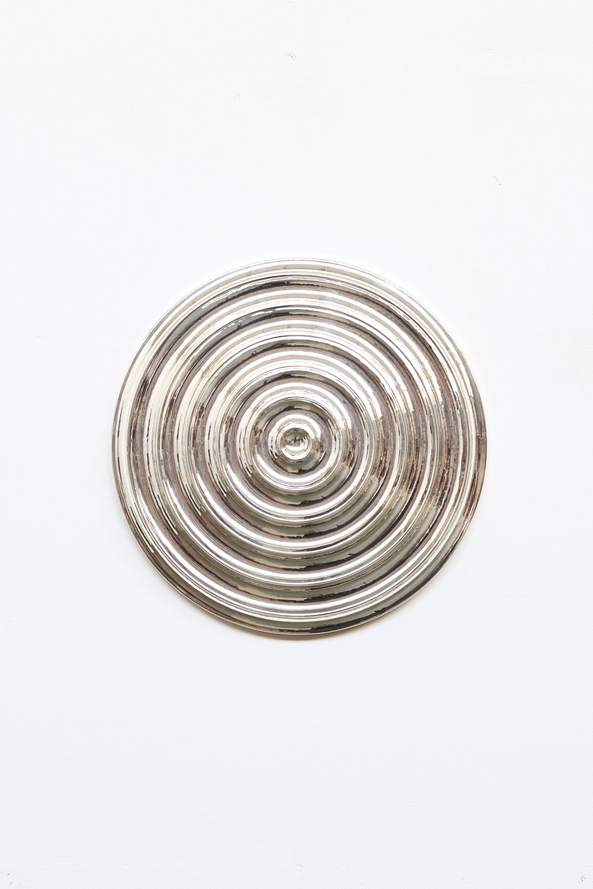 The Klaveroog by Studio Arno Hoogland is a shiny, metallic circular object with concentric raised rings, centered on a plain white background. Its Wave Chrome Silver surface reflects light for a polished, mirror-like look.