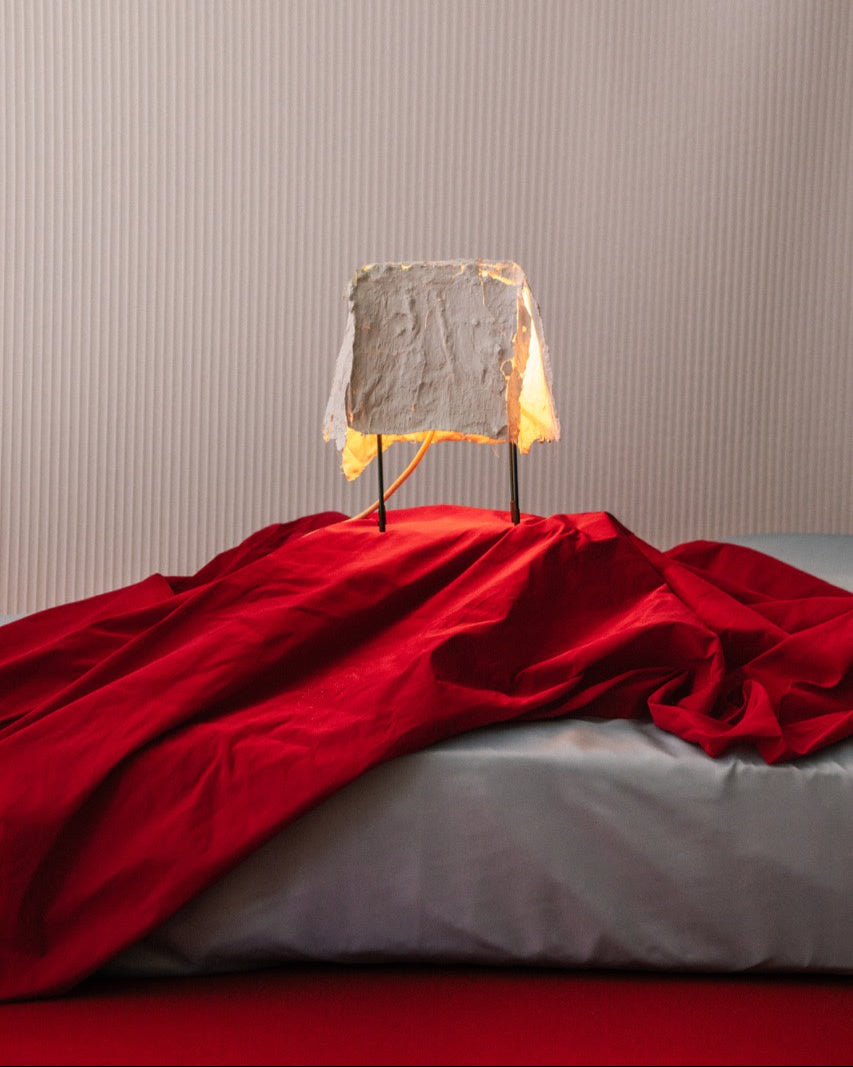 Contemporary table lamp with textured concrete shade on red fabric backdrop