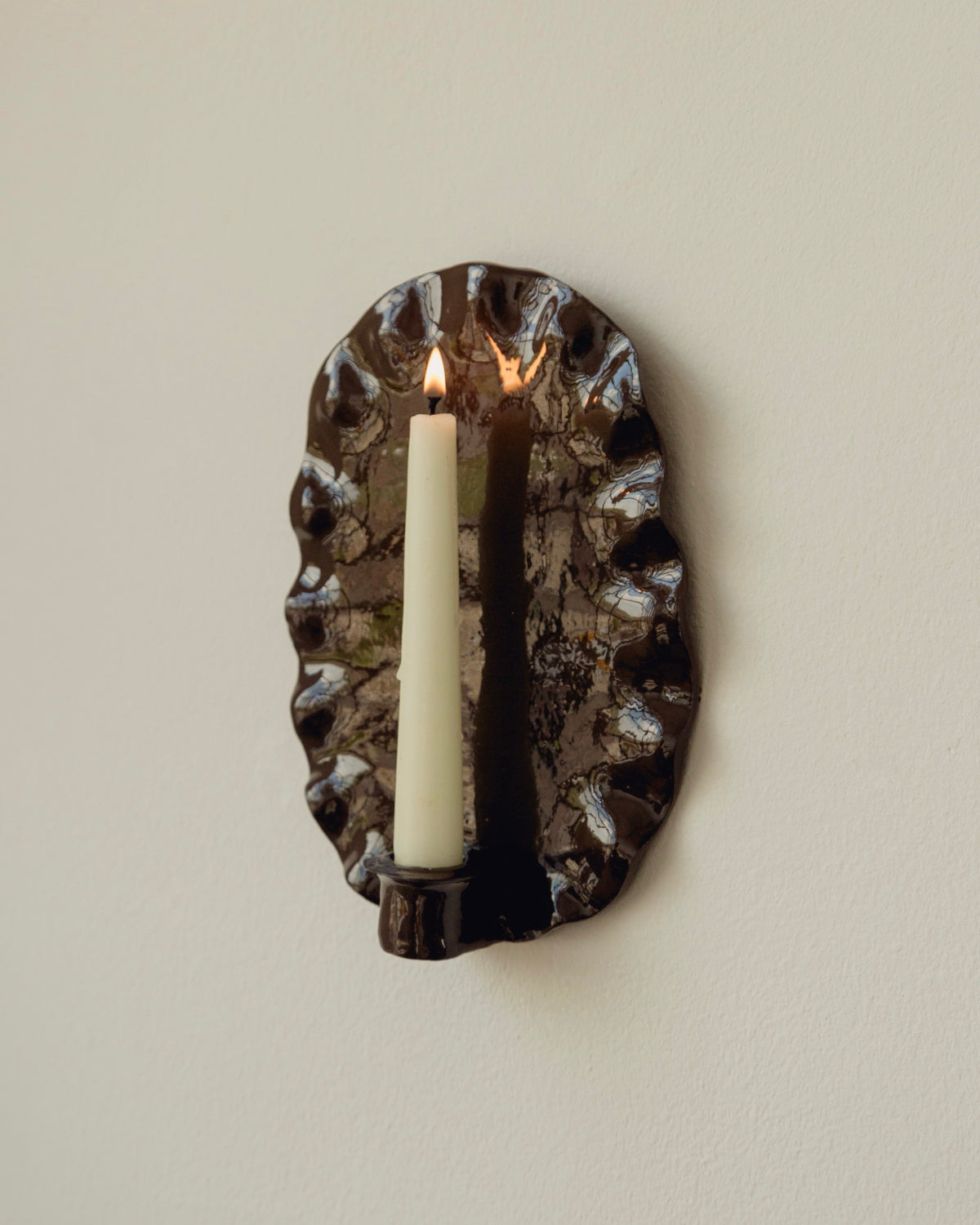 The Ortigia Candle Holders in Glazed Ceramic — close-up of dark ceramic with lit candle