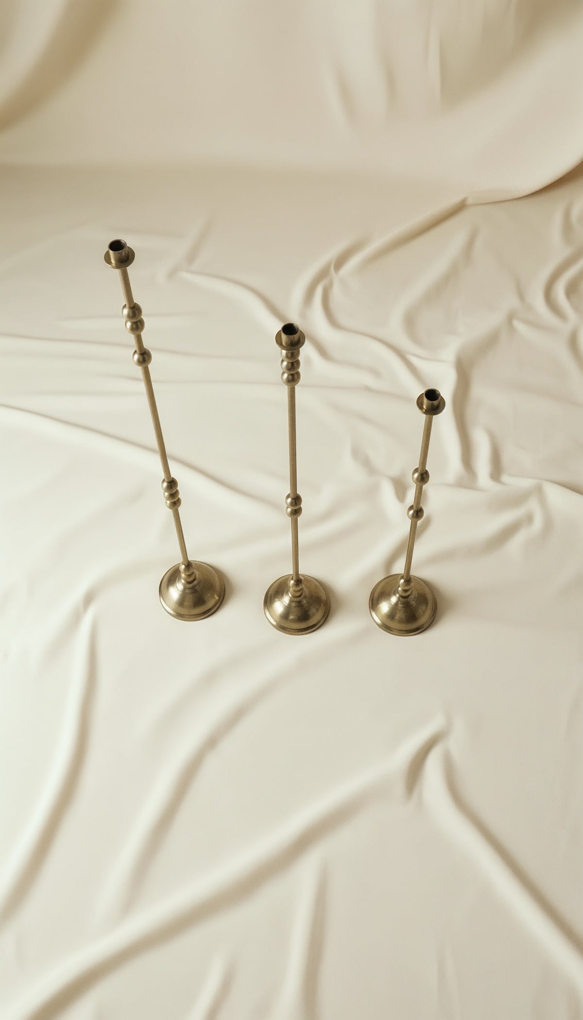 ASHA I – Brushed Brass Sculptural Candlestick Set — top view on soft fabric background