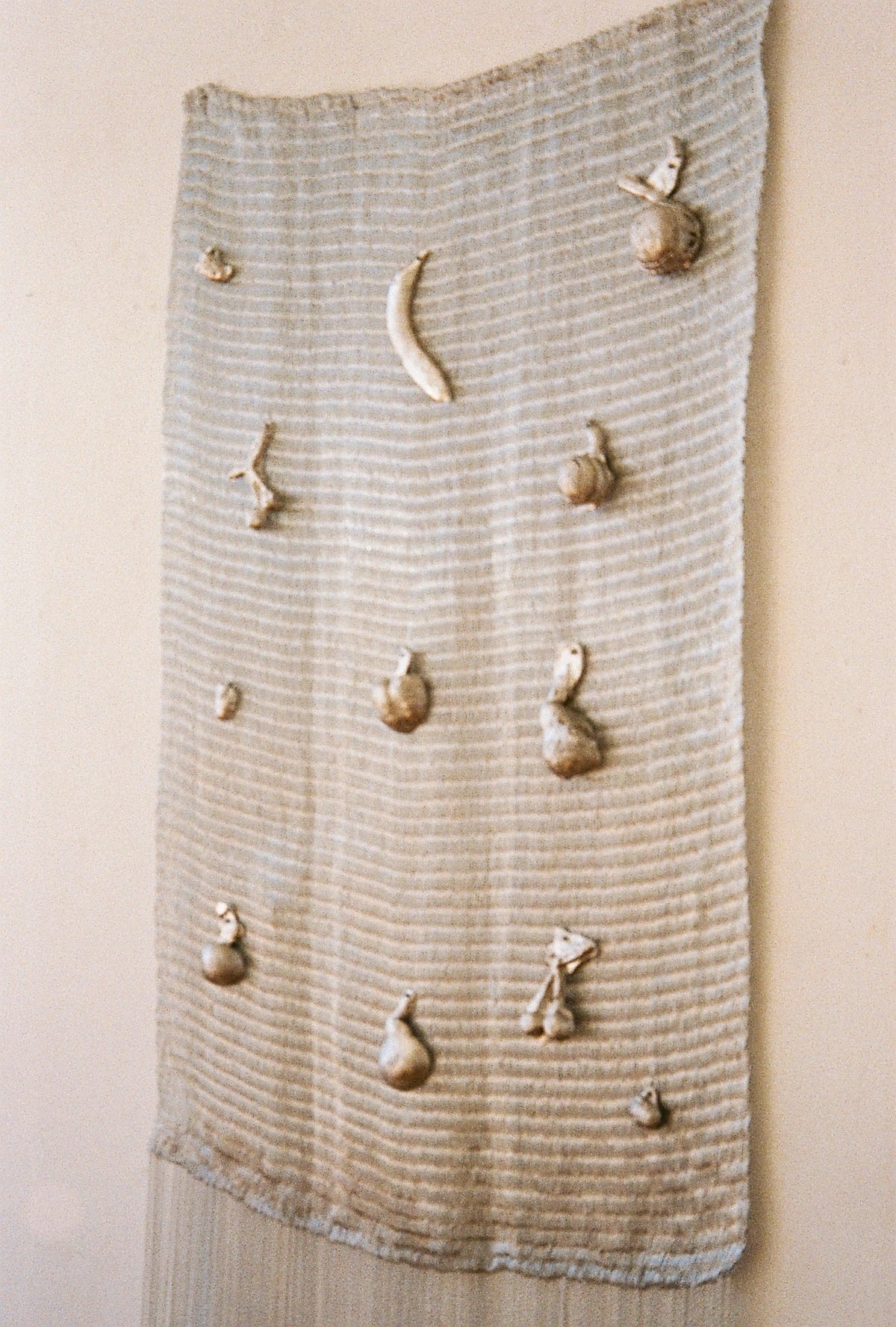 Textured wall sculpture with ceramic fruits and crescent moon on striped fabric