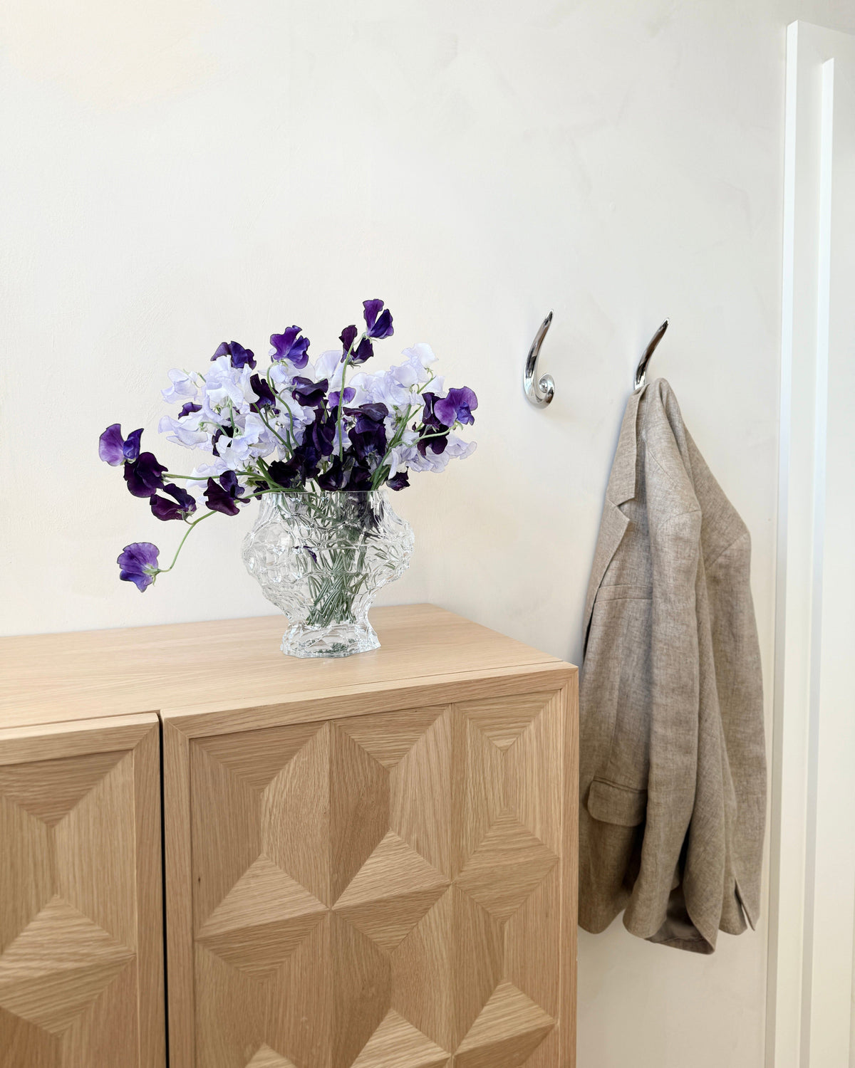 Noelle Hook - Brass — back view with coat and vase on wooden cabinet