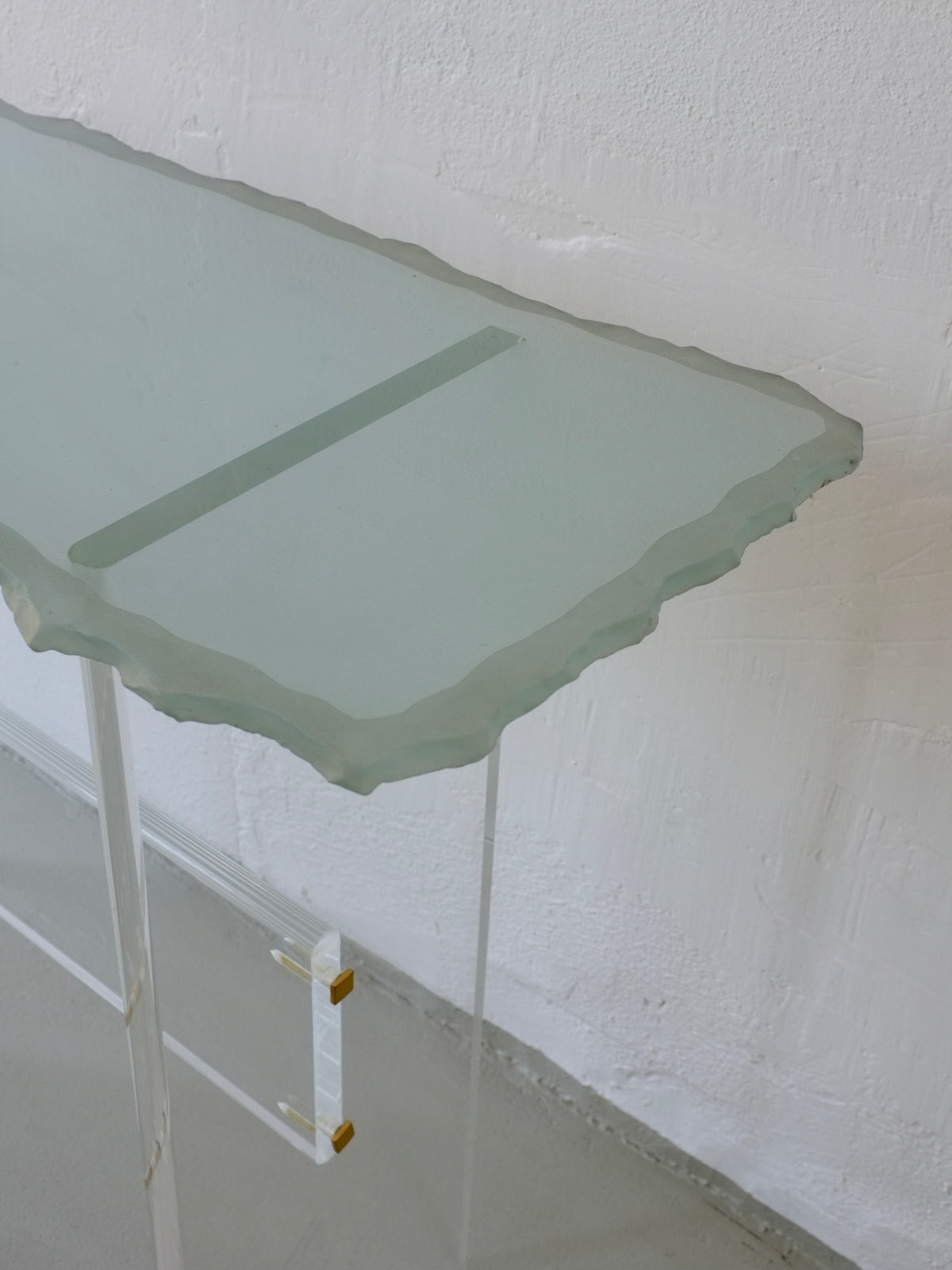 Sculptural glass console table with Lucite legs, corner detail view