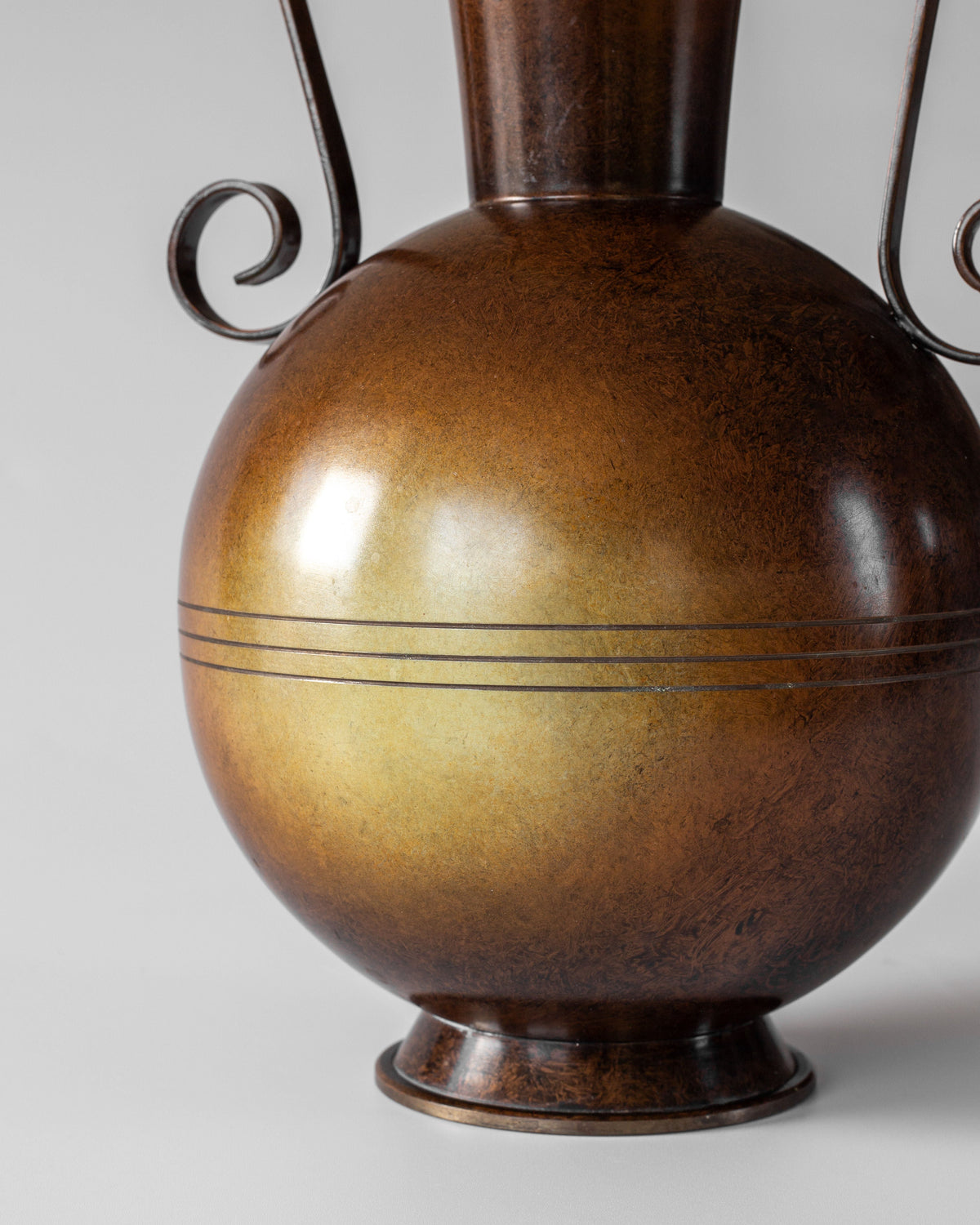The Spigel Swedish Art Deco Bronze Vase features a round shape, narrow neck, curled handles, and three engraved lines for an elegant touch, beautifully highlighted against a plain light background.