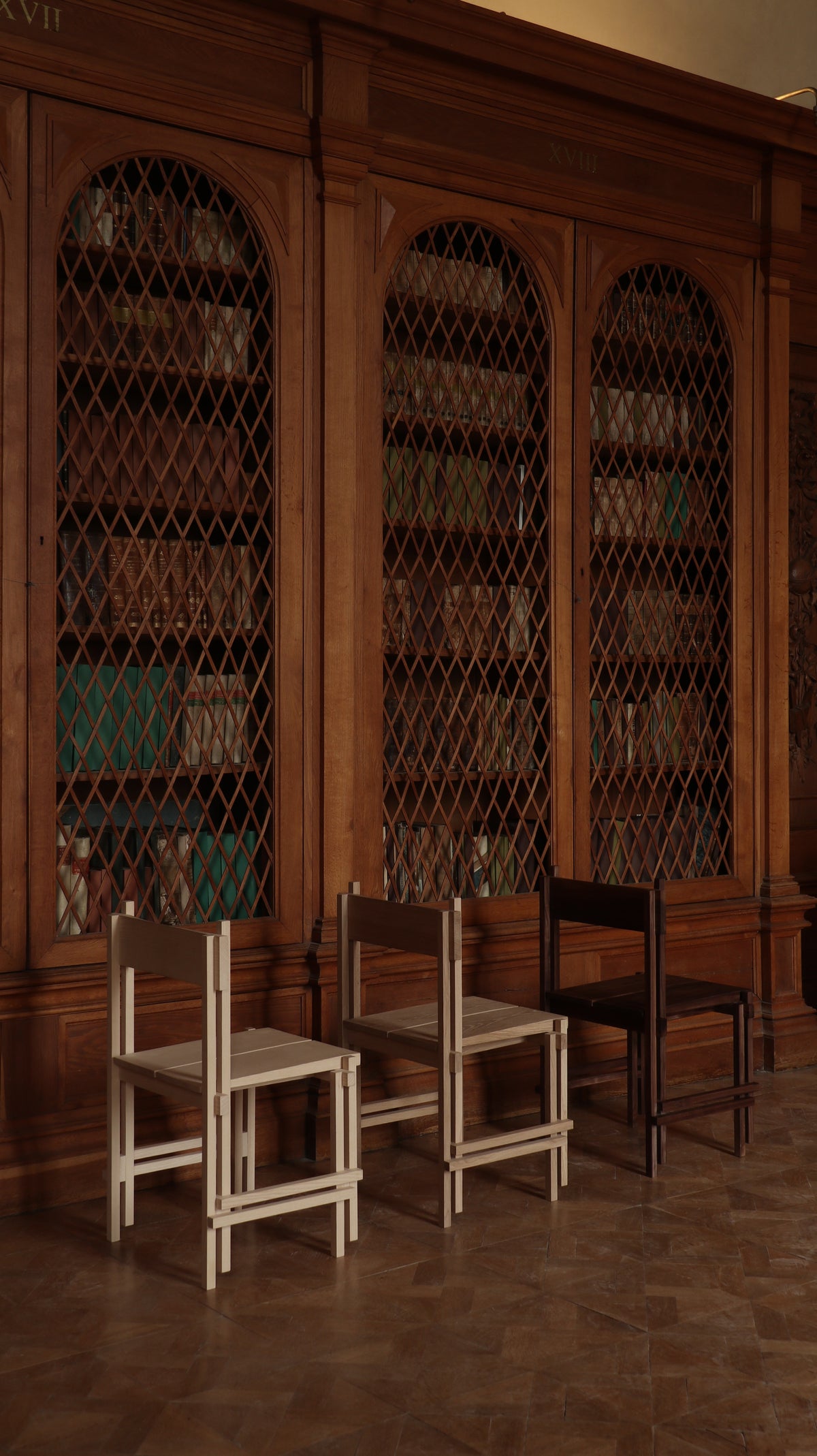 Minimalist stackable wooden chairs displayed against ornate library