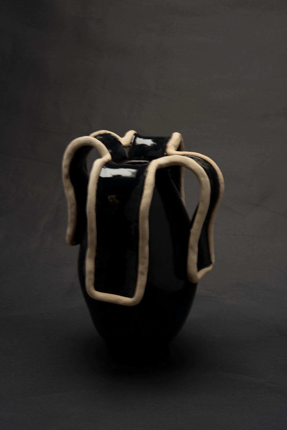 Glossy black ceramic vase with sculptural cream clay handles detail