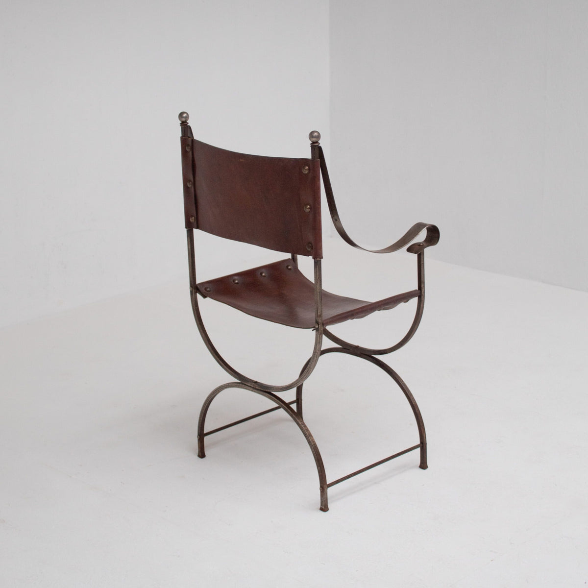 French pair of Iron Curule Chairs in Leather — angled view highlighting leather seat and iron frame
