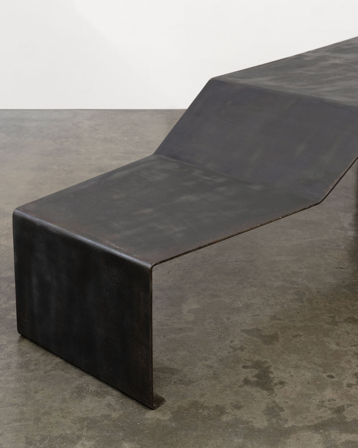 Large patinated steel bench with angular backrest profile view