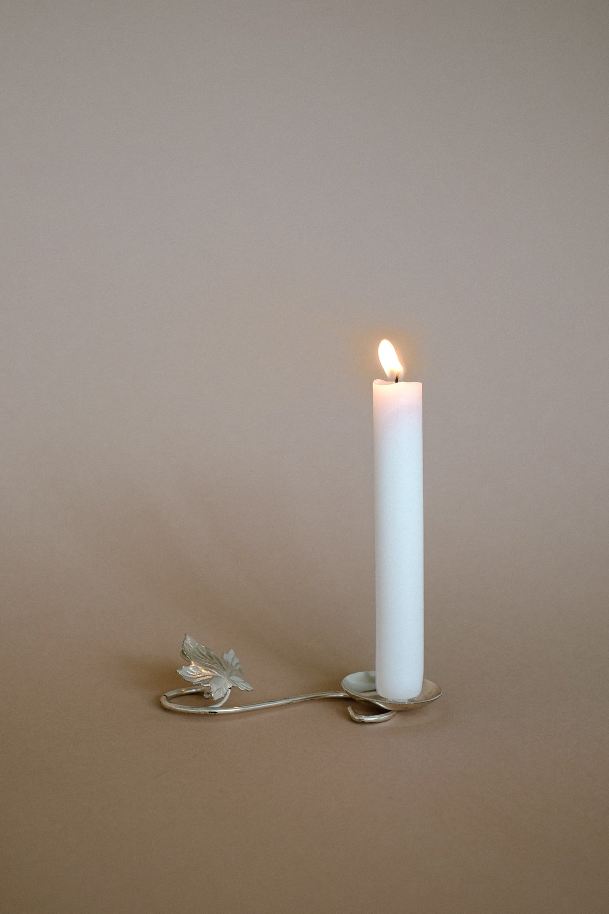 Silver-plated candle holder with decorative leaf detail and lit candle