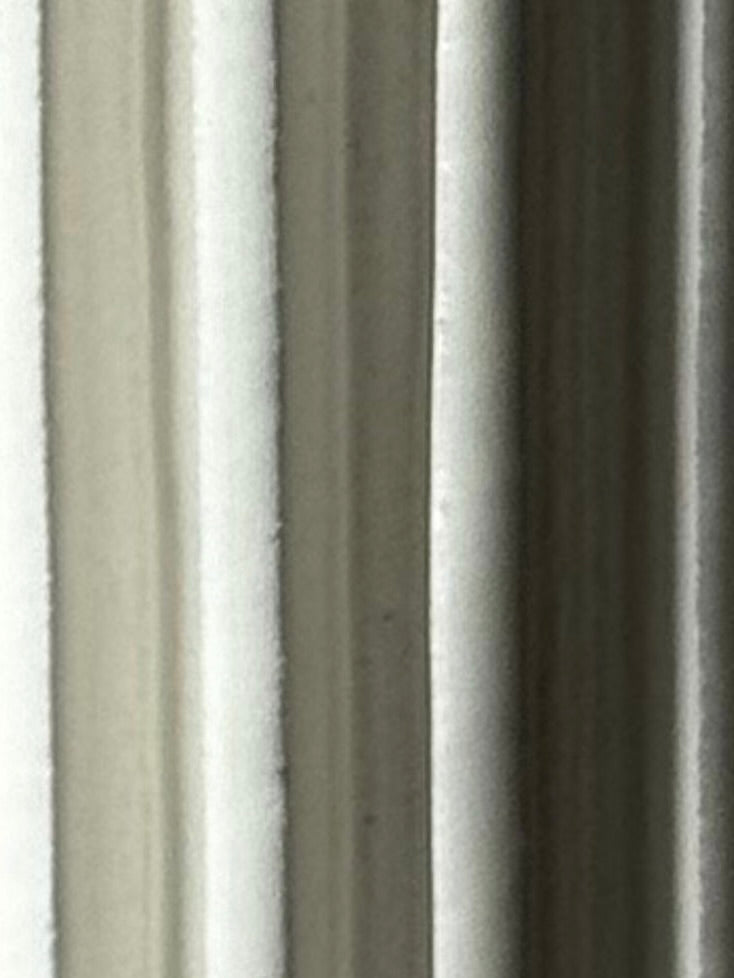 Close-up of softly folded, light-colored fabric curtains with gentle shadows, forming an abstract neutral-toned pattern evocative of Vessel No. V by Devin Wilde.