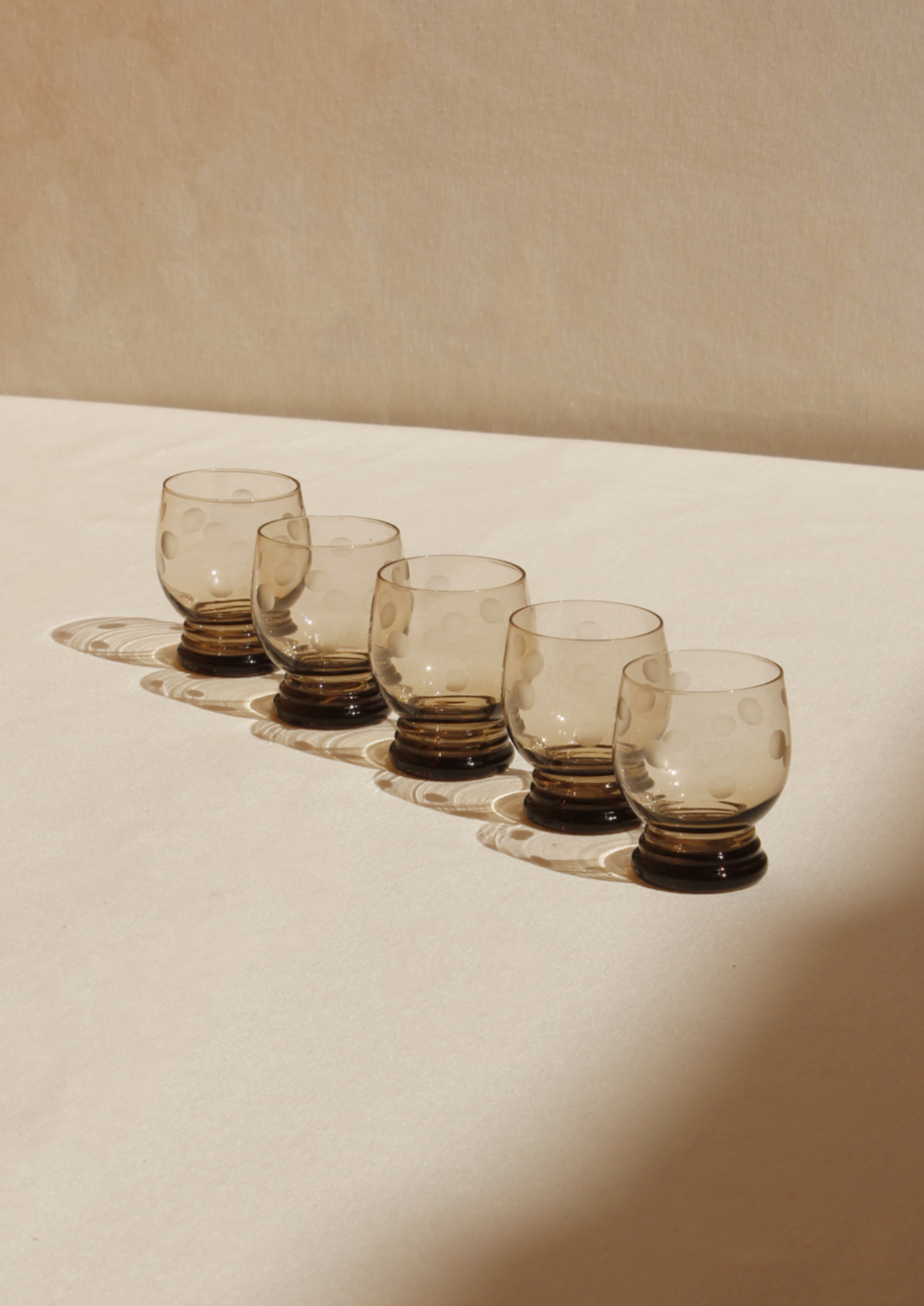 Five vintage Boga Avante Shop Polka Dot Glasses arranged in a row on a white ceramic tray, casting soft shadows on a neutral-toned surface.