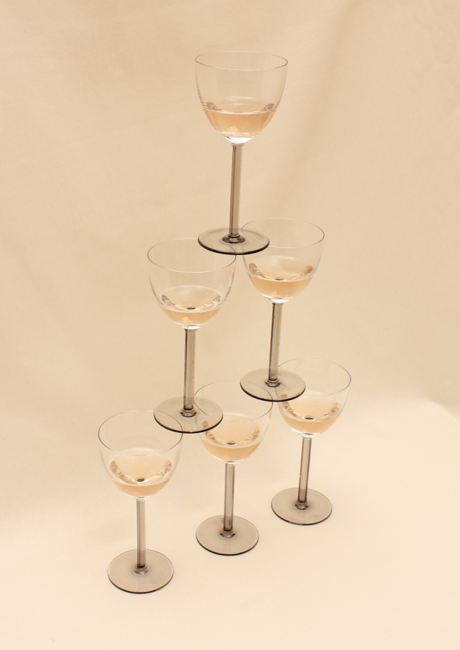 A pyramid crafted from six glasses of the Crystal Wine Glass Set by Boga Avante Shop stands against a plain white backdrop, exuding a minimalist aesthetic.