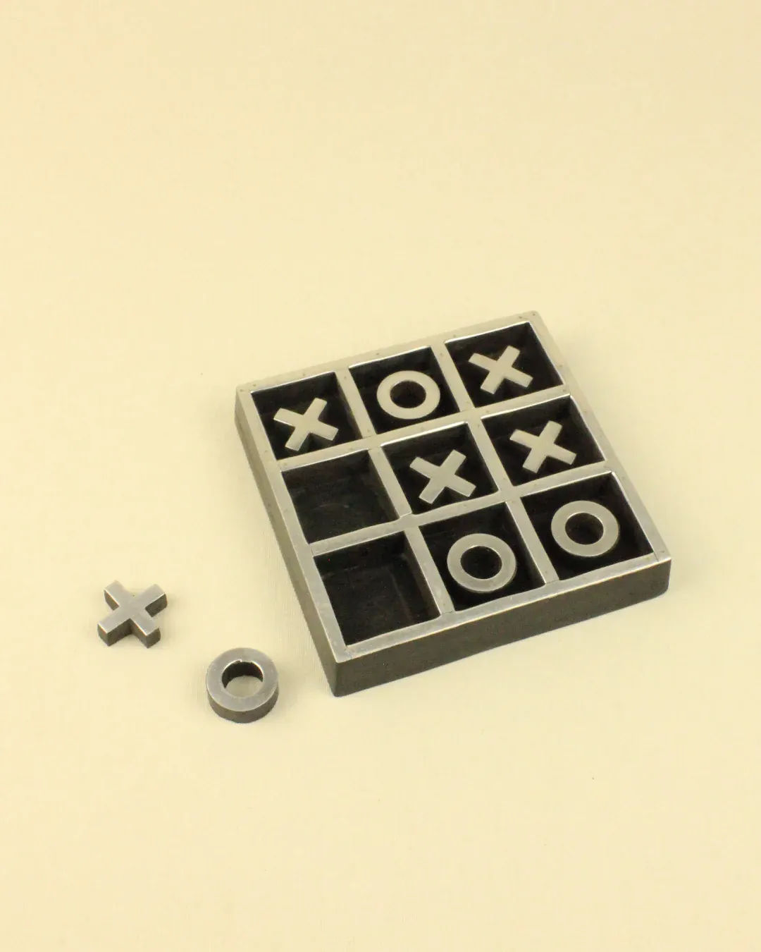 A Vintage Tic Tac Toe Game board with xs and os placed in various squares, one o piece and one x piece lying beside the board on a light background. Produced by Boga Avante Shop.