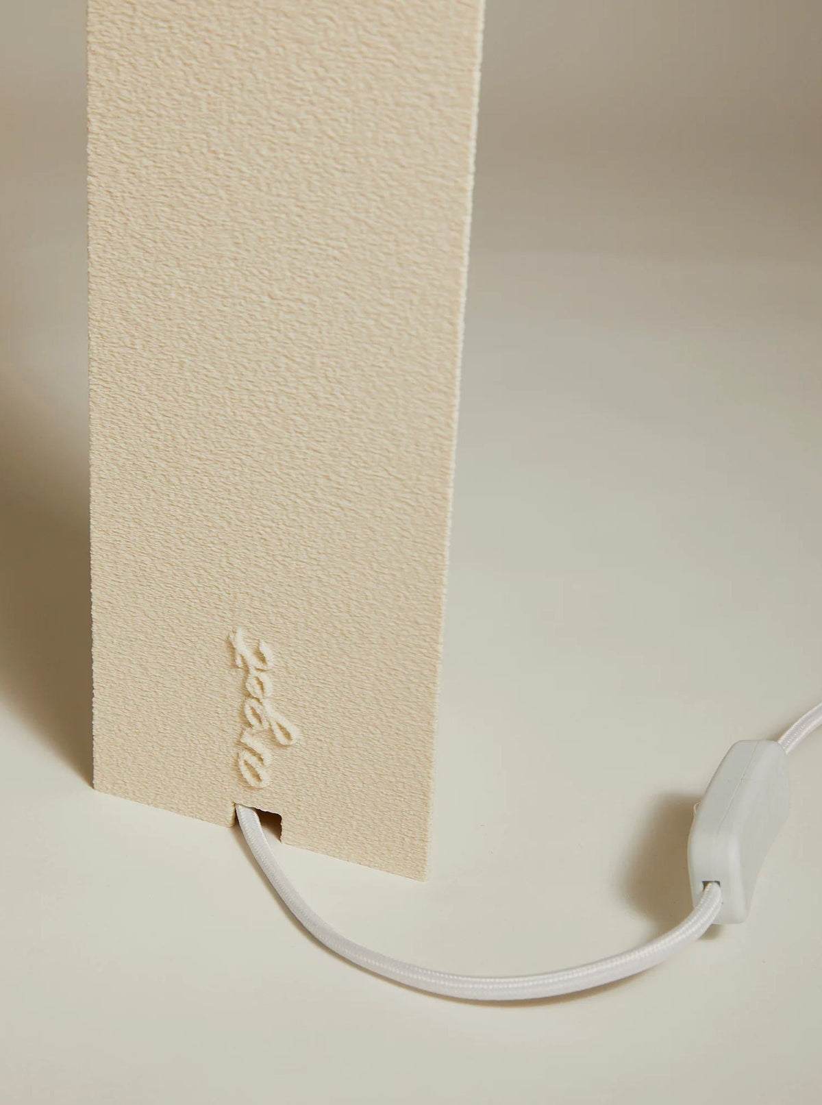 A close-up of a beige, textured Lampe ii charging station by Argot Studio with a minimalist Japanese design and a white cable plugged in at the bottom.