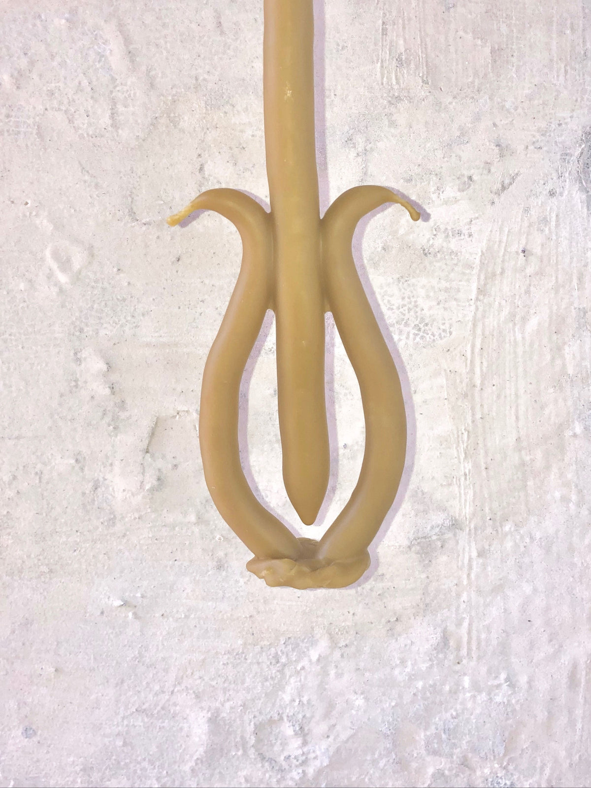 A close-up image of a hand-dipped Ola Lewczyk Candle 036 shaped like an abstract tulip, with melted wax forming delicate petals against a textured white background.
