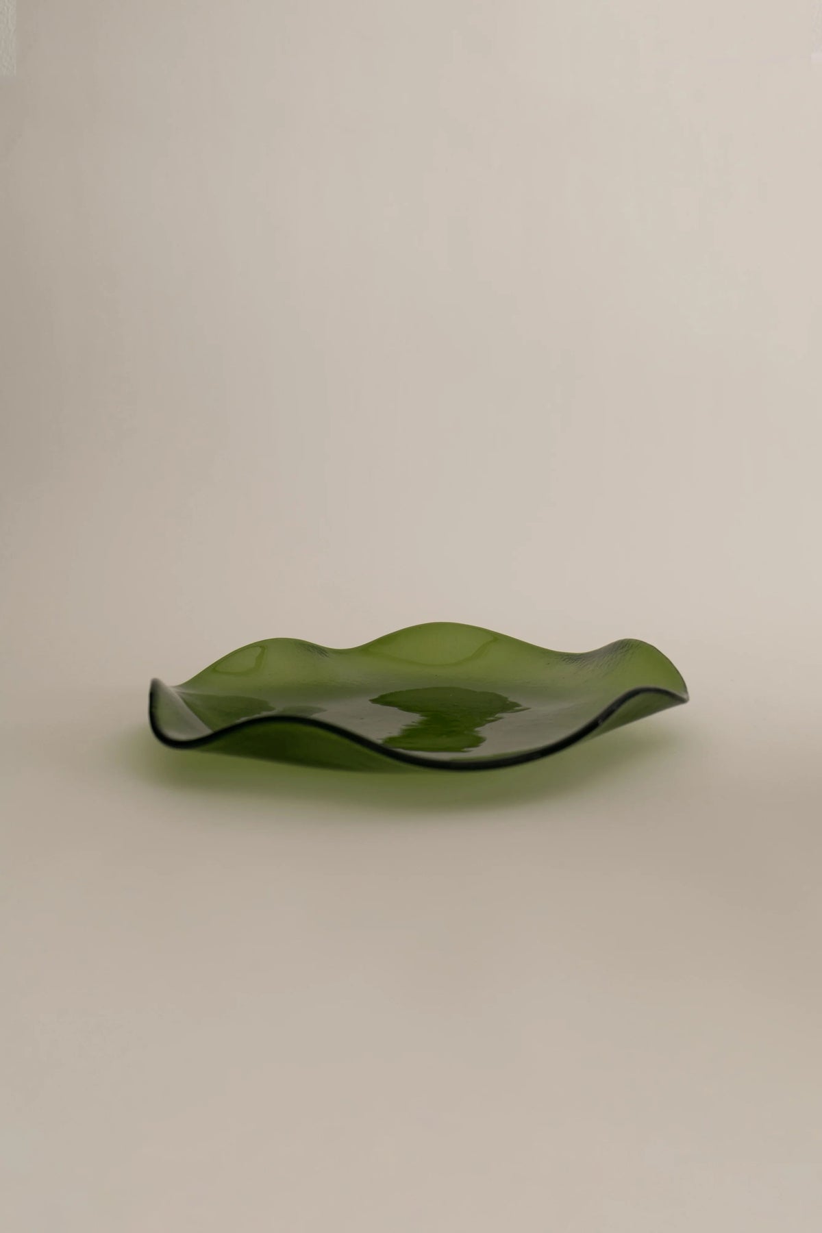 A green glass Sophie Lou Jacobsen Petal Plate - Large with a wave-like, undulating design, displayed against a neutral beige background.