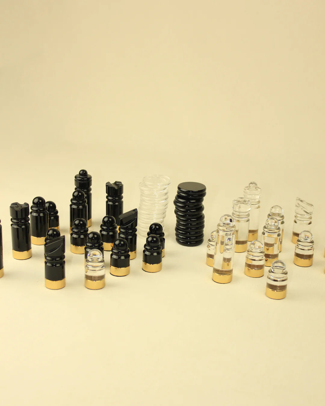 A collection of various small, empty cosmetic containers including bottles and jars in black, clear, and amber colors with brass accents, arrayed against a plain, light background.