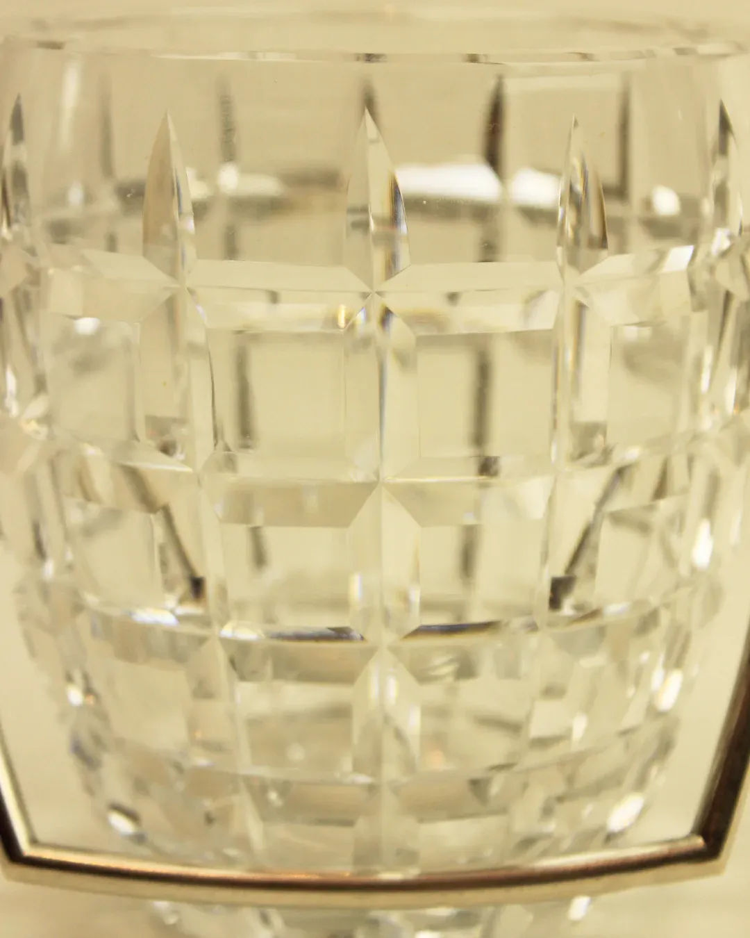 Close-up of the Crystal Cubitera from Boga Avante Shop, showcasing its clear crystal with a faceted, geometric pattern. This luxury accessory features a grid of rectangular and square cuts that reflect light to create intricate, sparkling reflections. The background is a soft, neutral color.