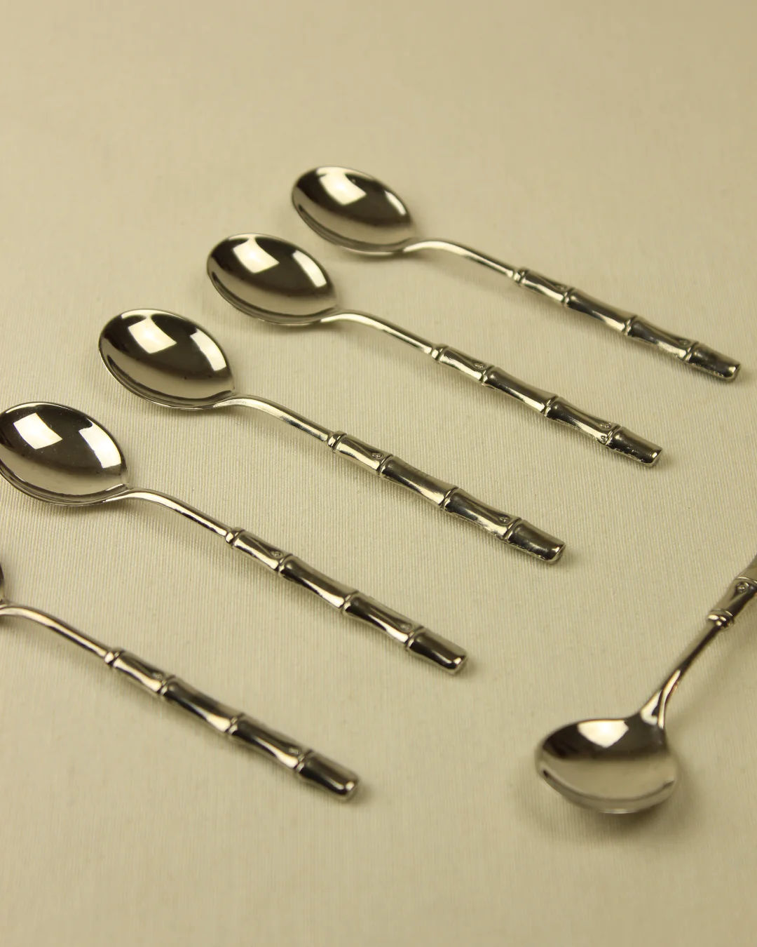 Five Bamboo Silver-Plated Spoons with elongated, twisted handles arranged in a diagonal line on a light beige background from Boga Avante Shop.