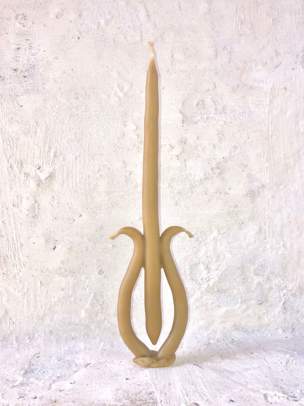 A unique Candle 036 by Ola Lewczyk, hand-dipped beeswax candle with an artistic, curvilinear design resembling a stylized letter "h," set against a textured white wall background.