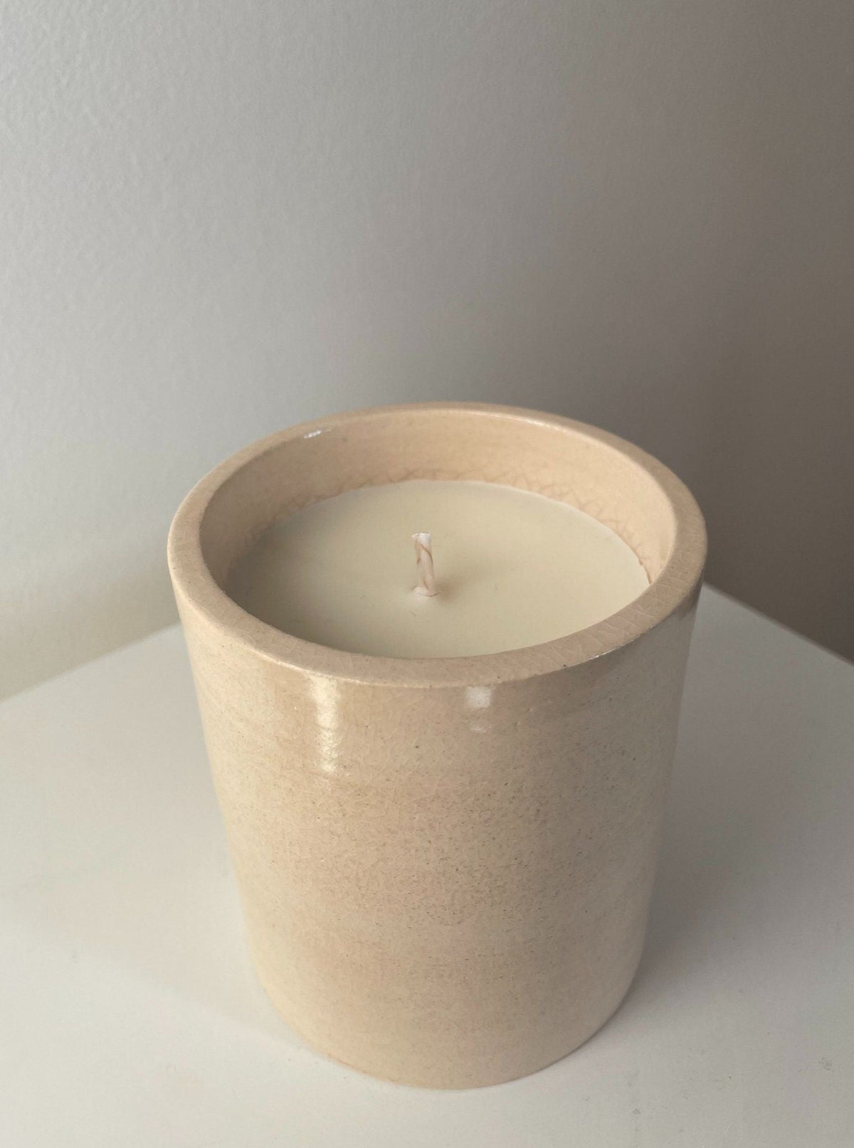 A beige ceramic Sculptural Scented Candle No. 11 from 2222Studio in a simple round container, placed on a white surface against a light grey background, highlighting the candle's wick and smooth wax surface.