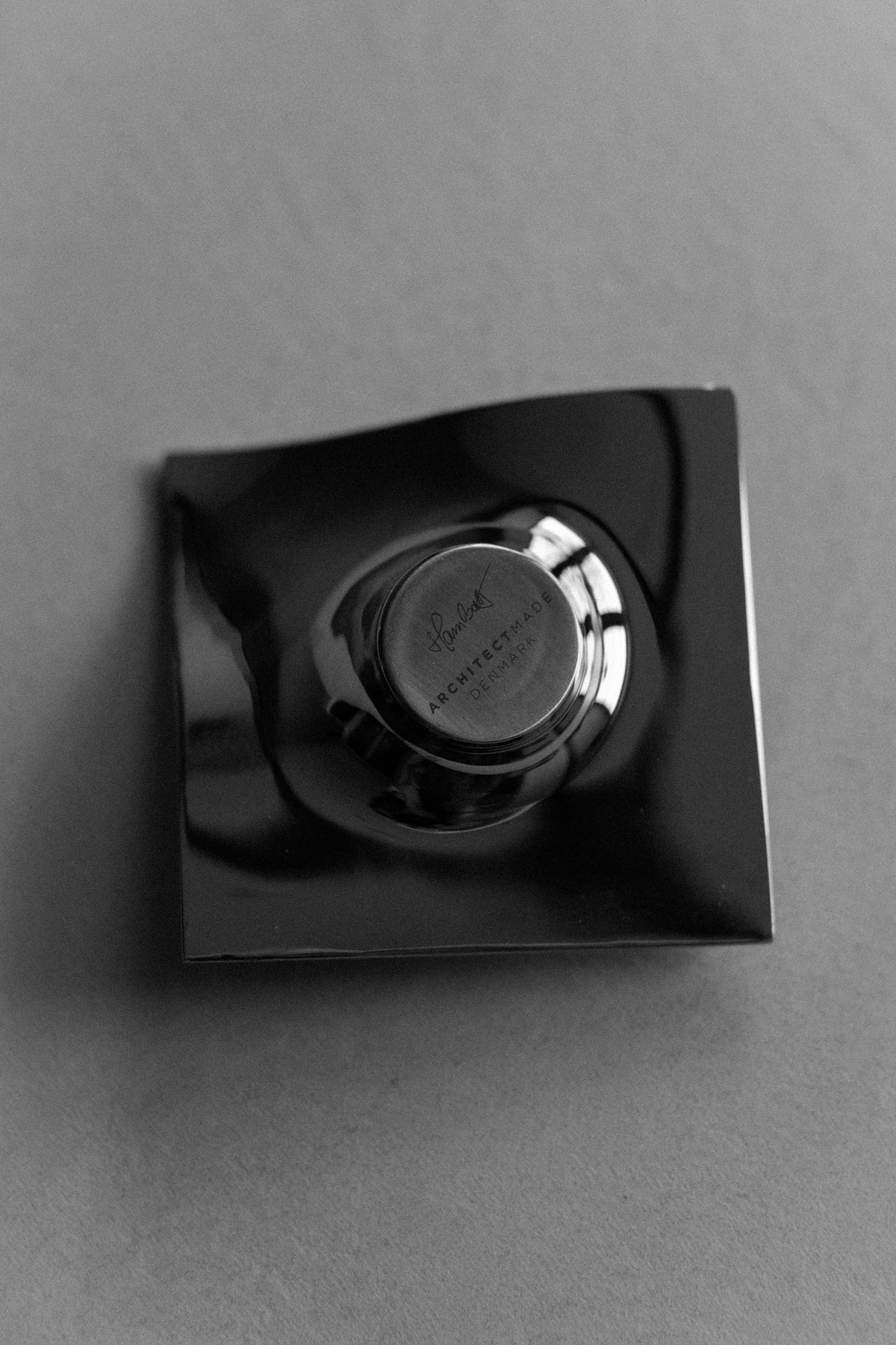 A black and white photo of a Out For Lunch 70's Chrome Candle holder, labeled "organic structures," placed on a glossy black surface that reflects its image.