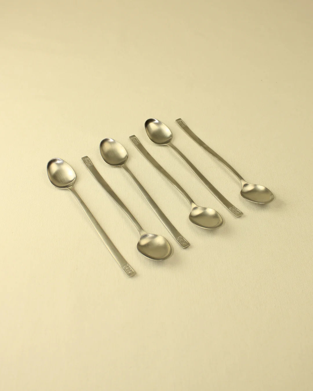 Six identical Boga Avante Shop 70s Style Spoons arranged diagonally on a pale beige background, alternating between bowl facing up and bowl facing down.