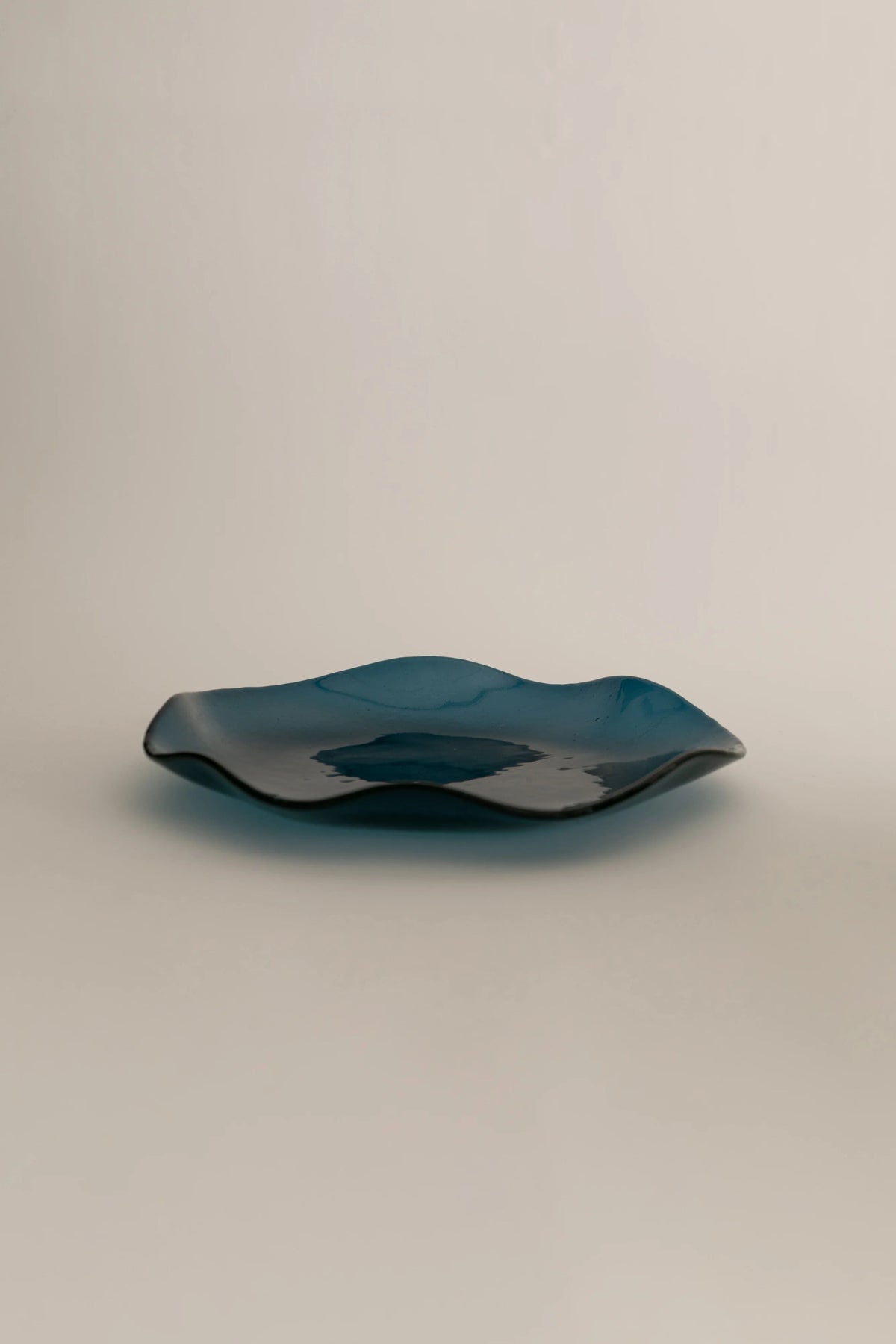A minimalist Sophie Lou Jacobsen Petal Plate - Large with an undulating, organic shape, crafted through an artisanal production process, displayed against a neutral beige background.