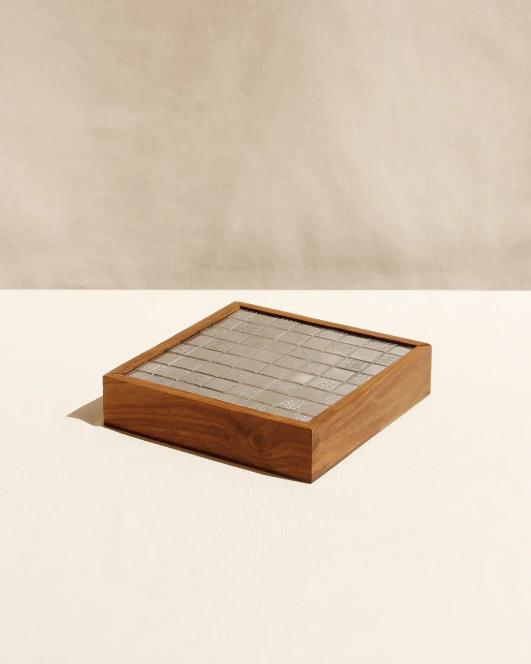 The Wood and Metal Chessboard by Boga Avante Shop sits on a beige surface with its stone-tiled design exuding luxury. A textured wall in the background enhances its contemporary aesthetic.