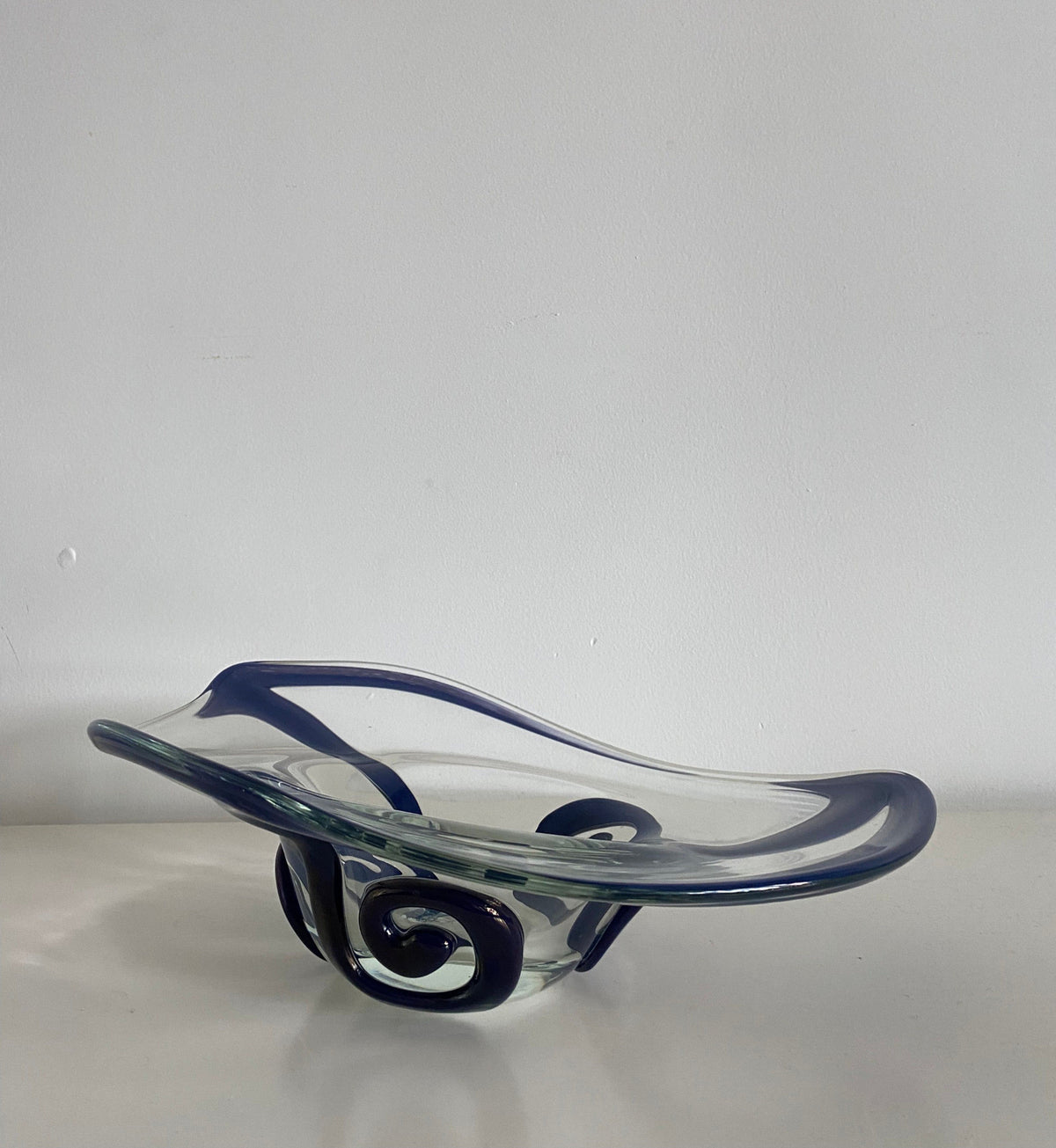 A modern 1998's Czech Bowl from Les Objets Amsterdam with exquisite craftsmanship, featuring a unique swirling design and irregular shape, placed on a white surface against a white wall.